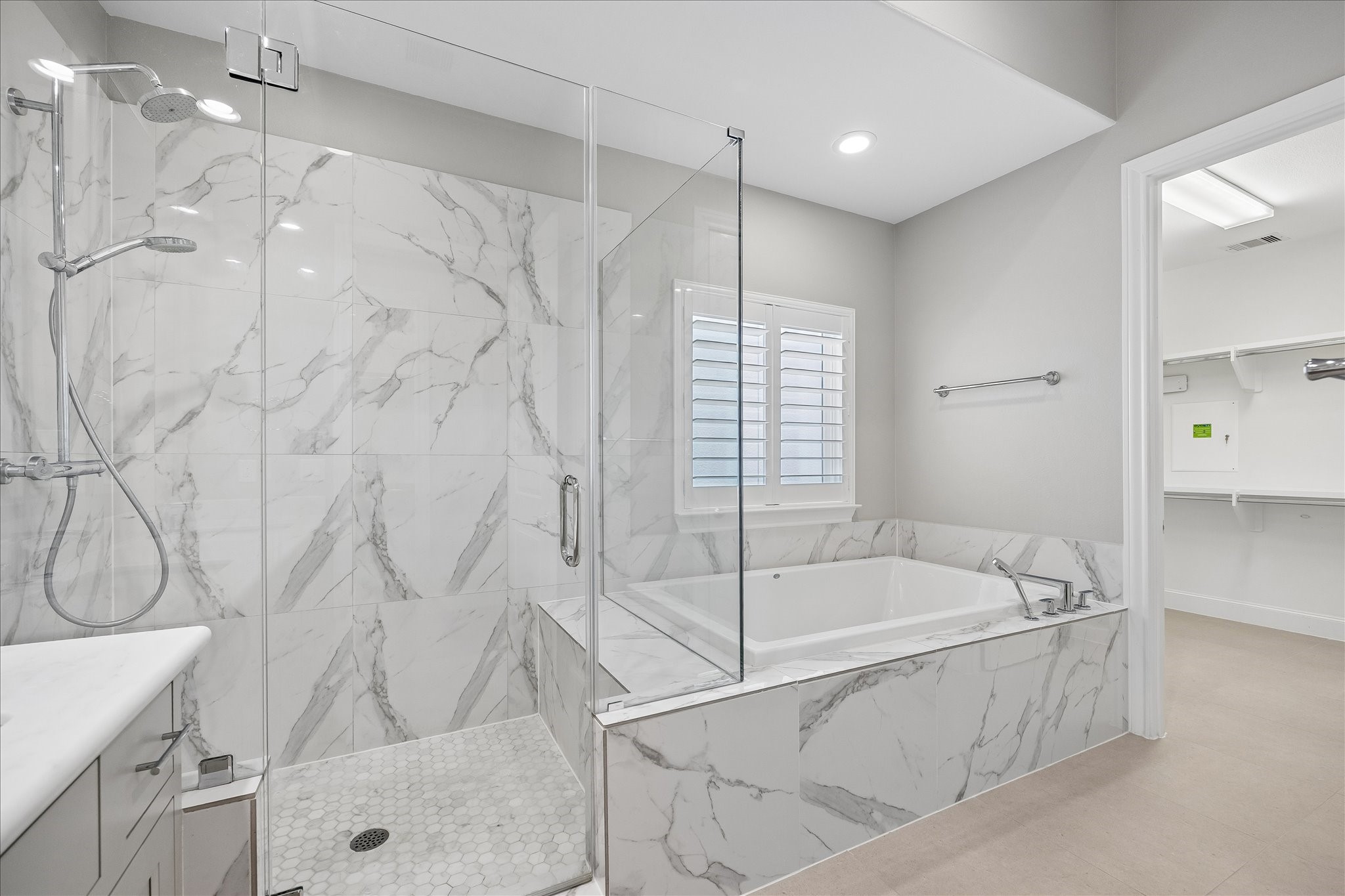 Luxurious bathroom with elegant marble tiles, featuring a spacious glass-enclosed shower and a relaxing soaking tub beneath a bright window.
