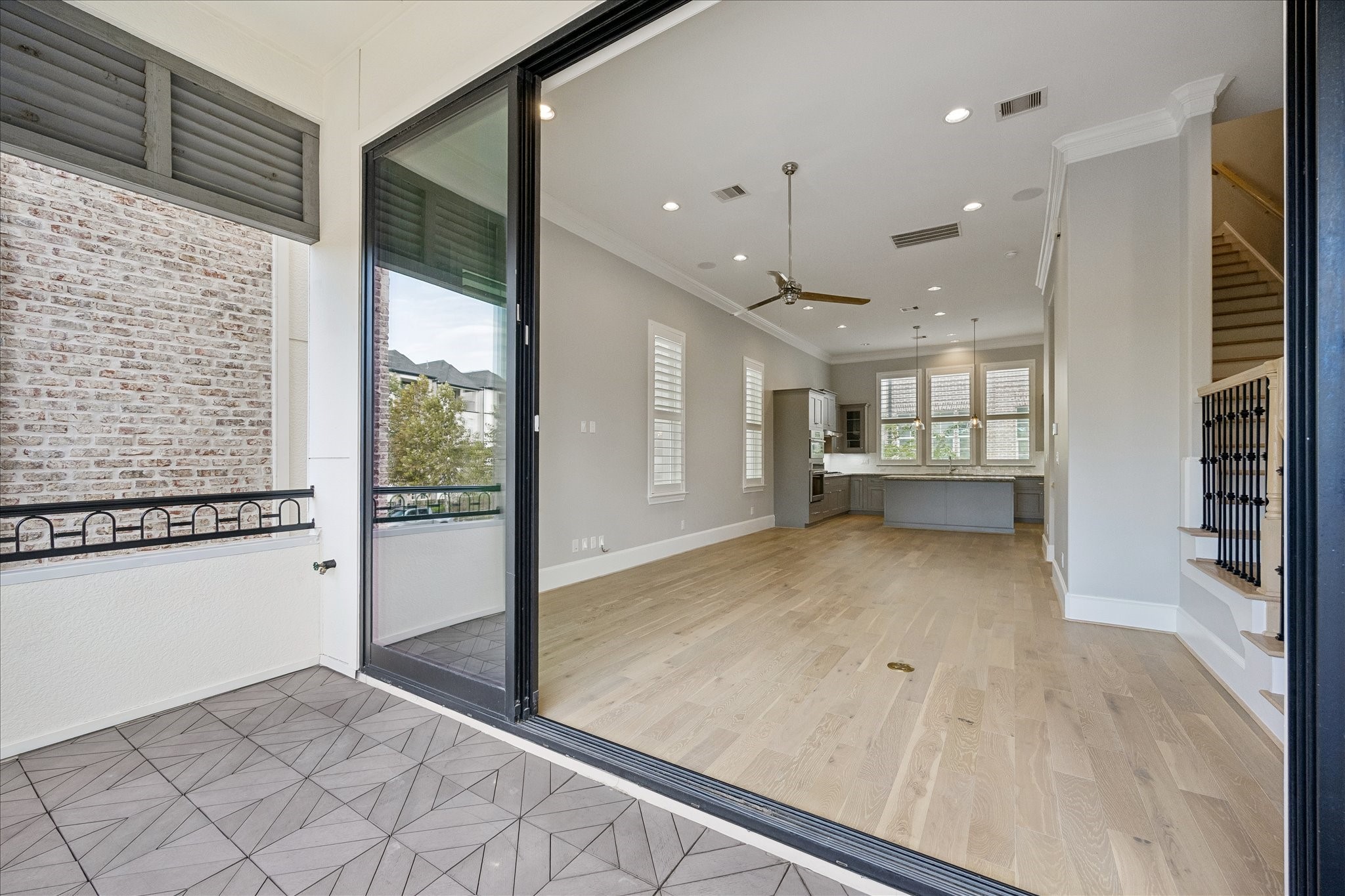 Spacious open-plan living area with elegant hardwood floors, modern kitchen, and ample natural light, seamlessly extending to a charming tiled balcony.