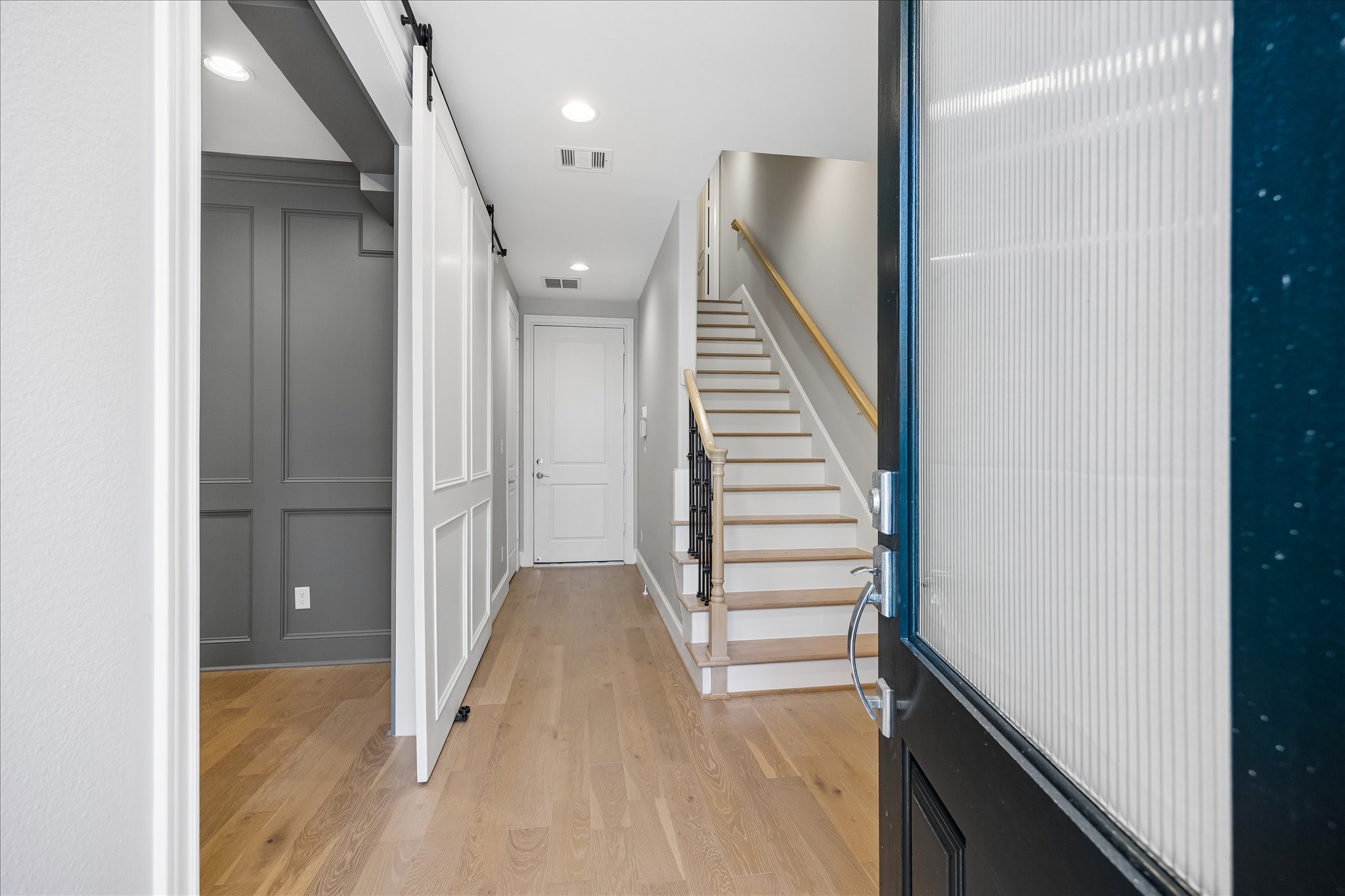 Inviting entrance with sleek hardwood floors, a modern sliding barn door leading to downstairs bedroom or office, and a staircase leading to the upper level.