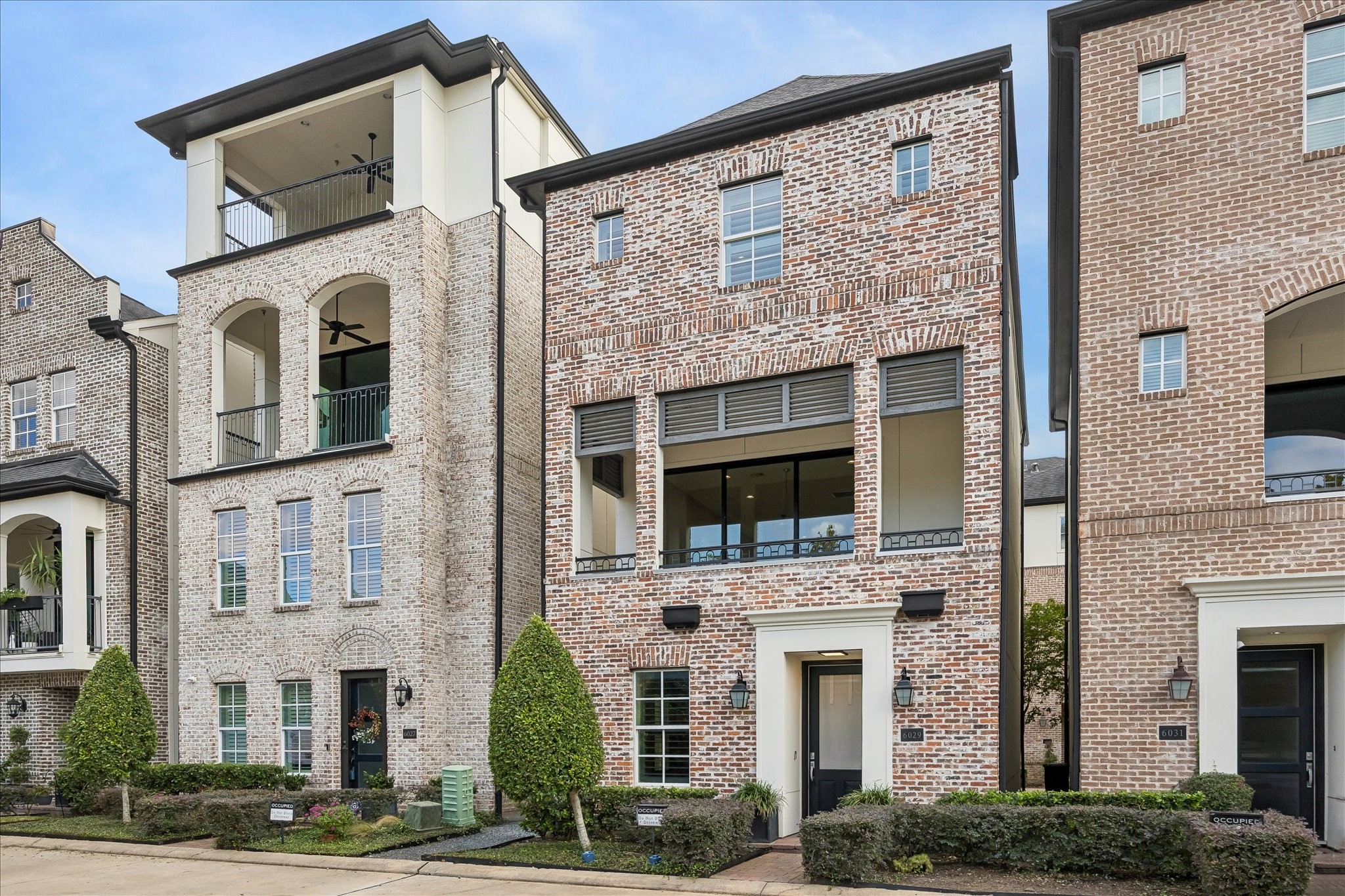 Elegant 3-story single family home with a classic brick facade, large windows, and a charming covered balcony overlooking water and fountain.