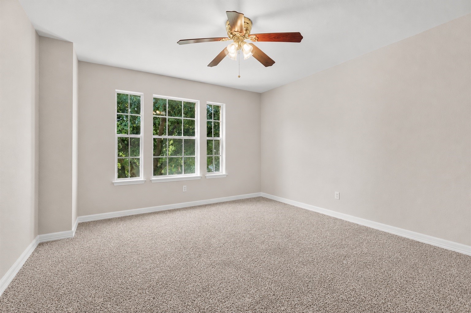 Secondary bedroom filled with natural light from multiple windows and overlooking mature trees.