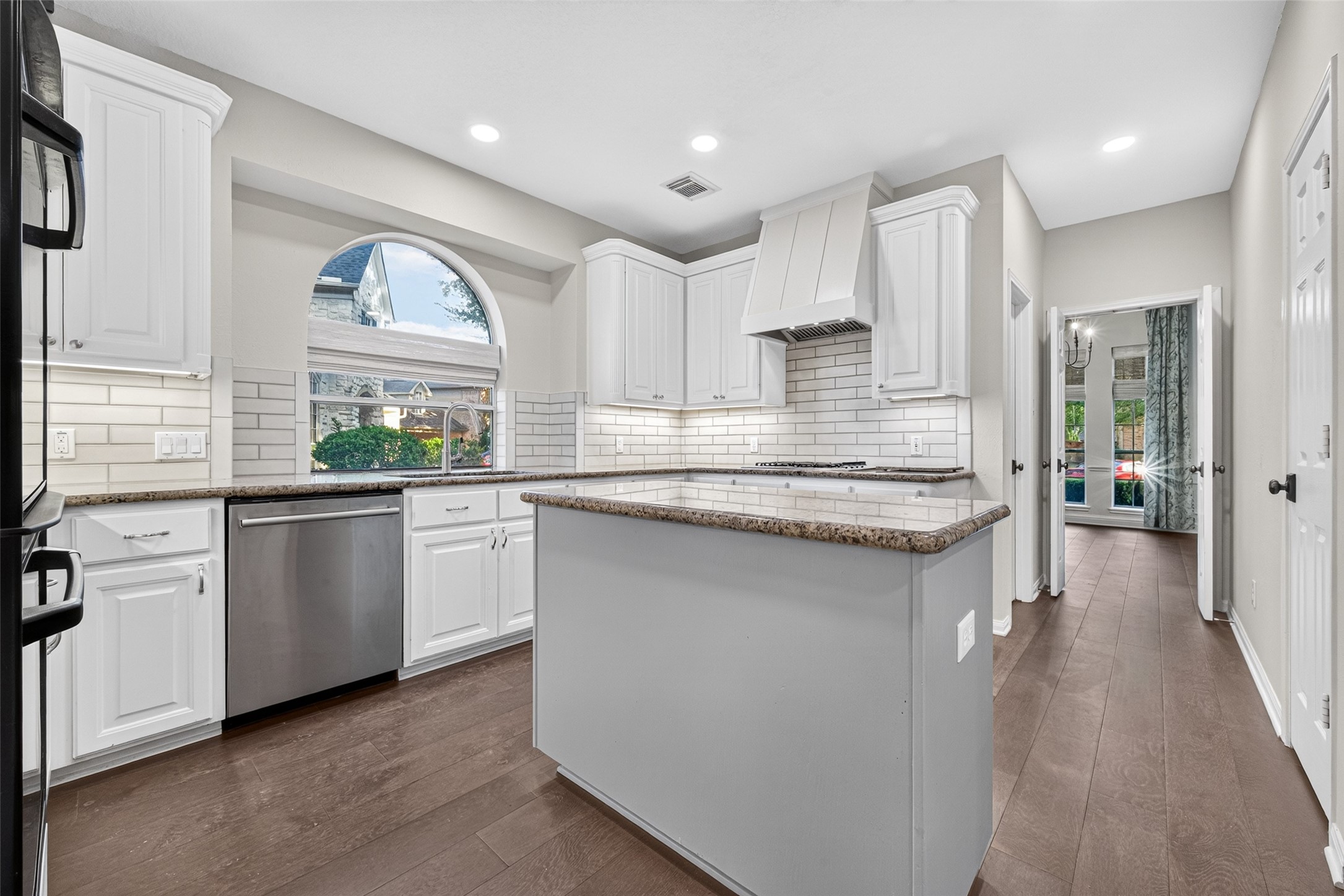 A KITCHEN DESIGNED FOR EVERYDAY LIVING! Bright white cabinetry, granite countertops, a subway tile backsplash & beautiful wood flooring create a welcoming space for preparing meals & gathering throughout the day. The center island provides additional workspace, while the arched window over the sink adds architectural character. Notice the recessed lighting, decorative vent hood & convenient access to the Formal Dining Room.