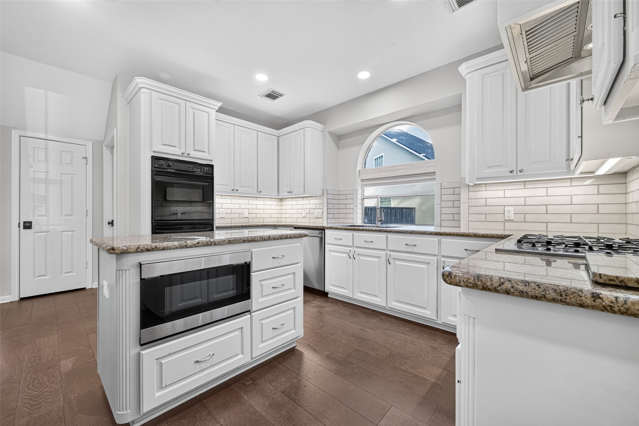 A KITCHEN THAT MAKES GOOD USE OF ITS SPACE! From this angle, you can appreciate how the island, double ovens, gas cooktop & sink are arranged for everyday convenience. The white cabinetry provides generous storage, while the granite countertops offer multiple preparation areas. Recessed lighting, undercabinet lighting & wood flooring complete the space.