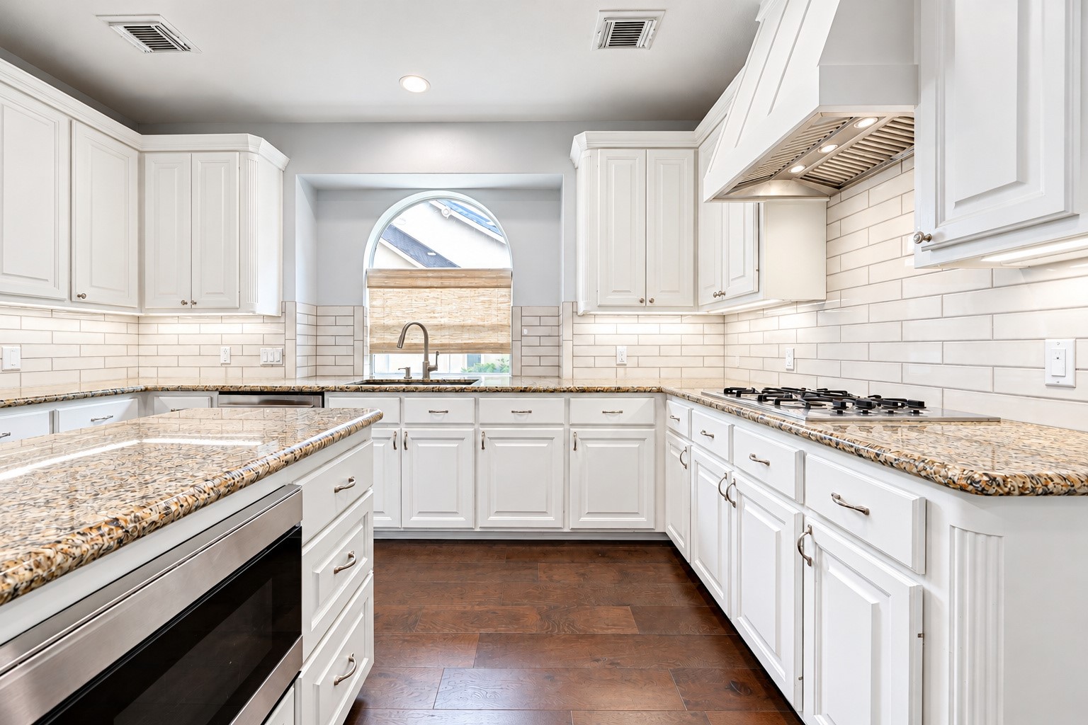 FOR THOSE WHO LOVE TO COOK! The gas cooktop sits beneath a decorative vent hood, surrounded by granite countertops & a crisp white subway tile backsplash. Gas cooking offers responsive temperature control, allowing you to move quickly from a gentle simmer to a rolling boil or adjust the heat while preparing your favorite recipes. With the center island nearby for chopping ingredients, organizing spices or setting out serving dishes, this thoughtfully arranged kitchen makes meal preparation enjoyable.
