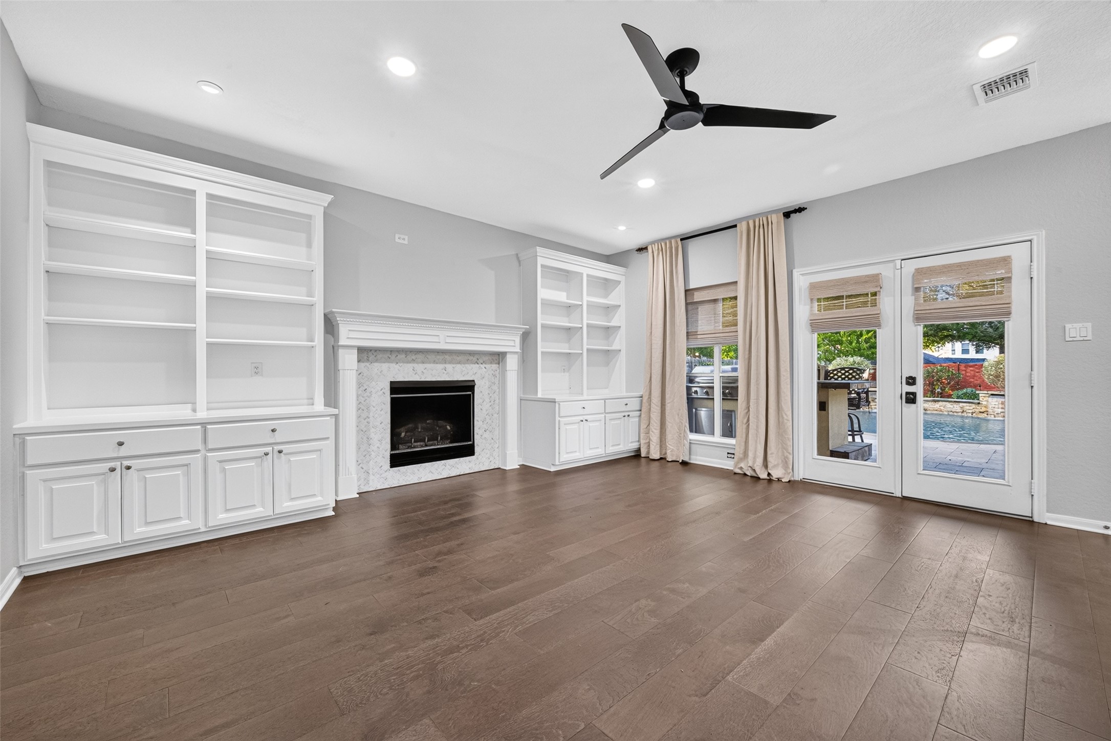 A BEAUTIFUL BACKYARD CONNECTION! French doors & tall windows bring the outdoors into view, offering glimpses of the sparkling pool & outdoor kitchen. The gas-log fireplace creates a welcoming focal point, while built-in cabinetry & shelves provide space for books, photographs & treasured keepsakes. Imagine cozy evenings by the fire or opening the doors to enjoy an afternoon of poolside entertaining.