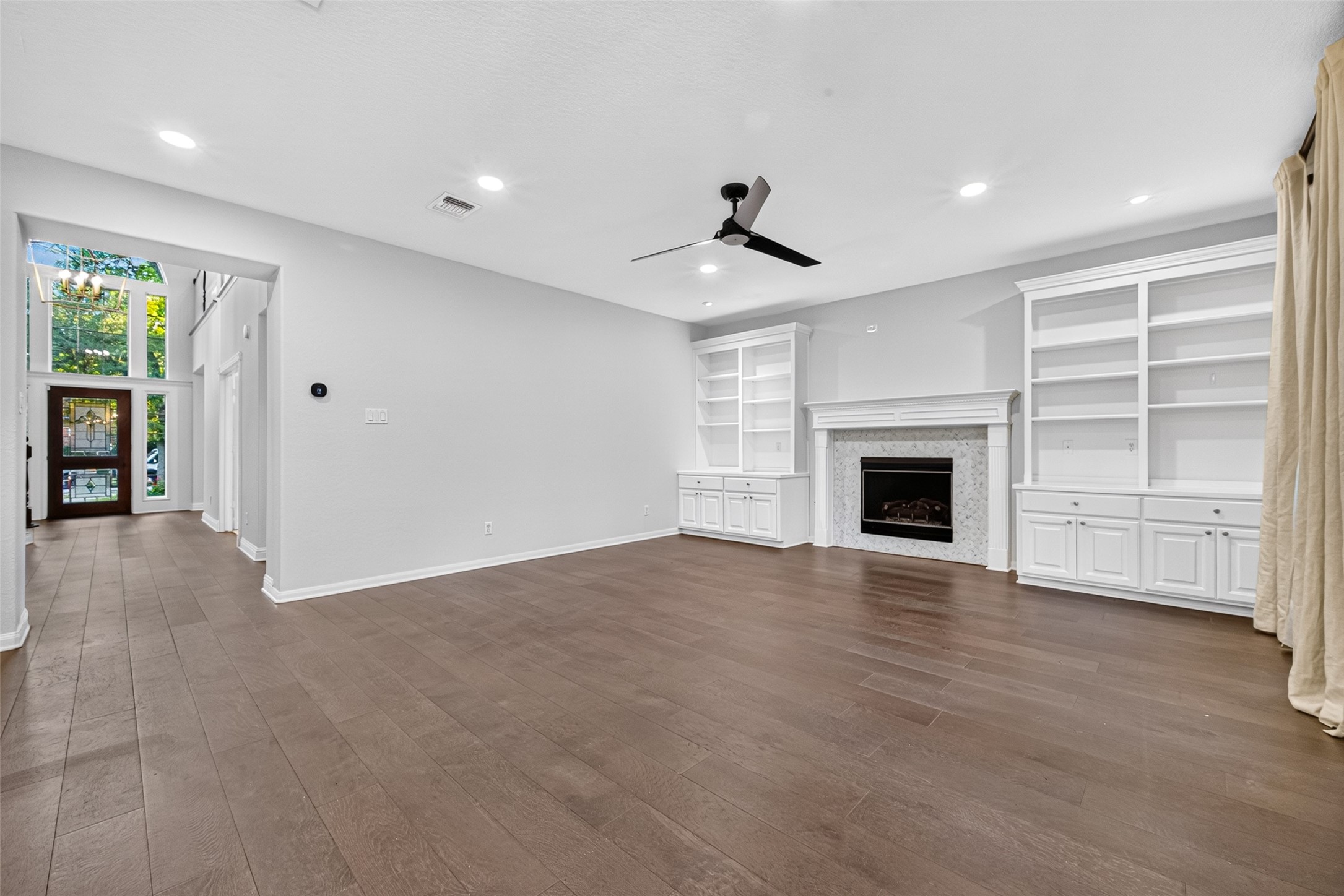 A FAMILY ROOM DESIGNED FOR COMFORT! Spacious & inviting, this Family Room features beautiful wood flooring, recessed lighting, a contemporary ceiling fan & a gas-log fireplace framed by white built-in cabinetry & display shelves. The generous proportions offer plenty of flexibility for arranging furniture, whether you prefer a large sectional for movie nights or separate seating areas for conversation. There's room to relax, unwind & make yourself at home.