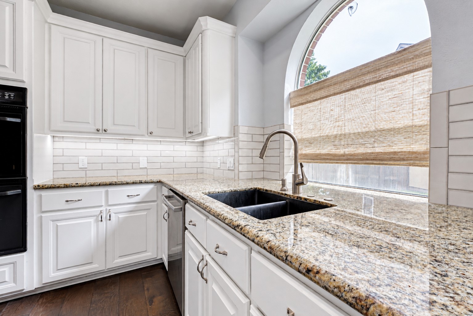 IT'S ALL IN THE DETAILS! The granite countertops provide generous workspace surrounding the undermount double-basin sink, while the gooseneck faucet makes everyday cleanup convenient. White cabinetry, subway tile backsplash & undercabinet lighting brighten the space. And that beautiful arched window? It's a lovely architectural feature that makes even washing dishes a little more enjoyable.