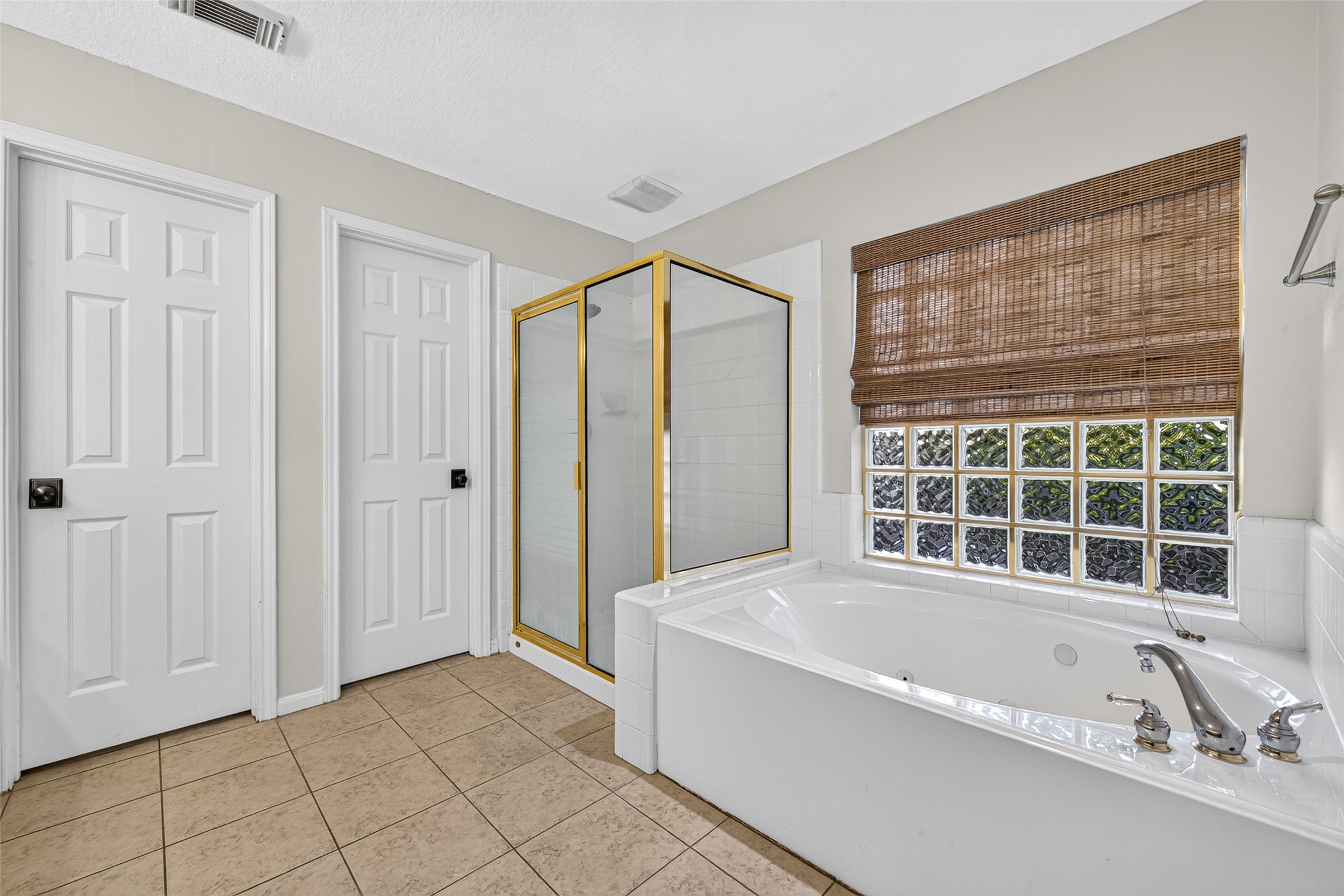 A LITTLE TIME TO RELAX & RECHARGE! After a busy day, imagine soaking in the jetted tub with a favorite book or enjoying a refreshing shower in the separate glass-enclosed shower. A glass-block window welcomes natural light while providing privacy, and a woven shade adds warmth to the space. With both bathing options available, this Primary Bath offers flexibility for a quick morning routine or a leisurely evening unwind.