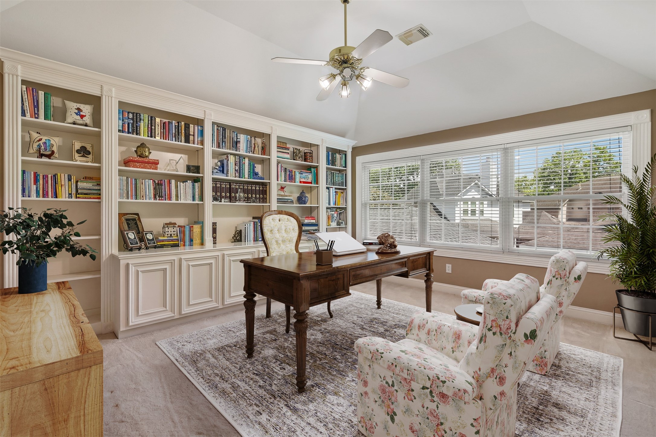 Upstairs game room features wall of built in bookshelves and cabinet space. There is a wall of windows for plenty of natural light as well as elevated ceiling with fan.
