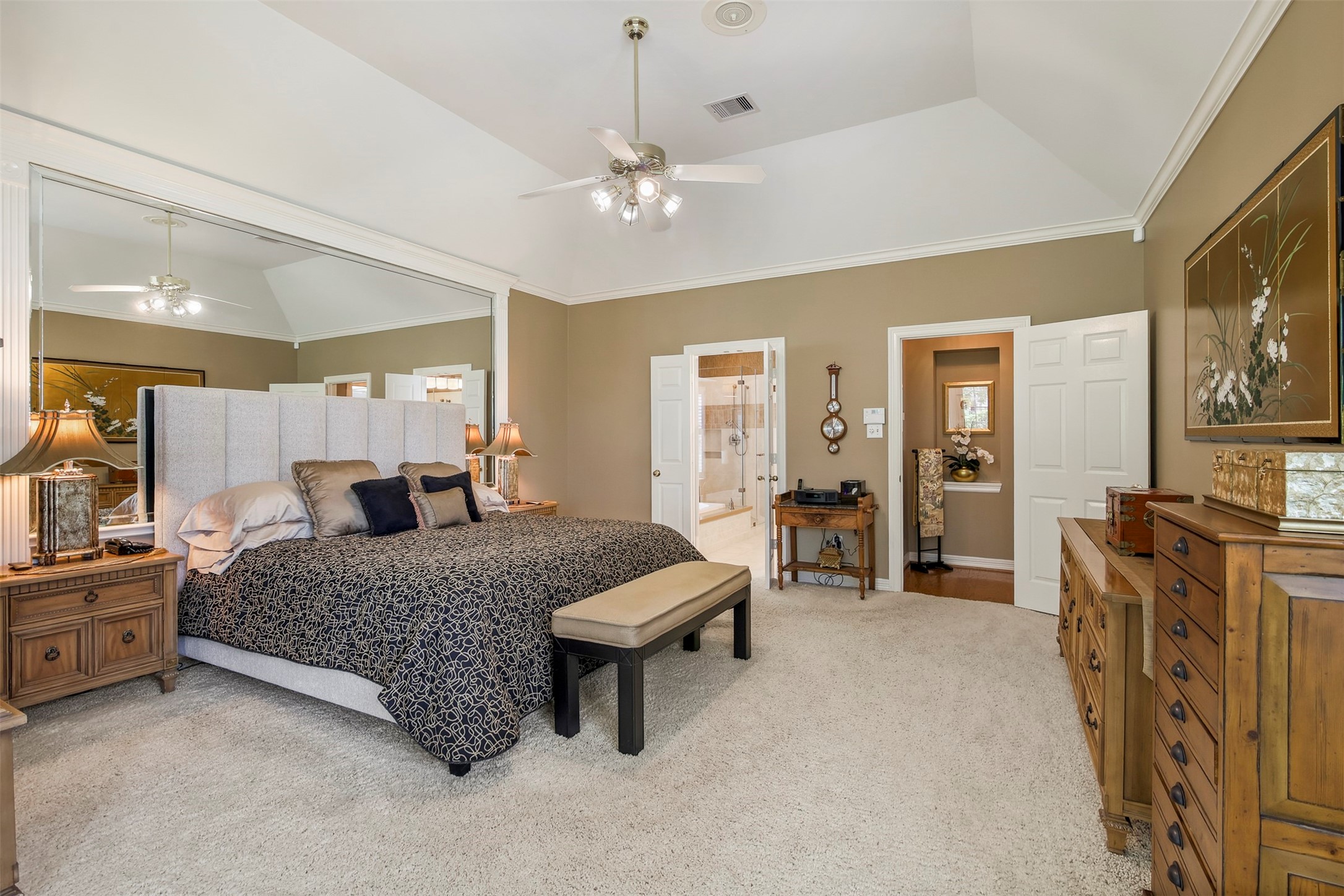 Another view of the primary bedroom with crown molding and large mirrored wall.
