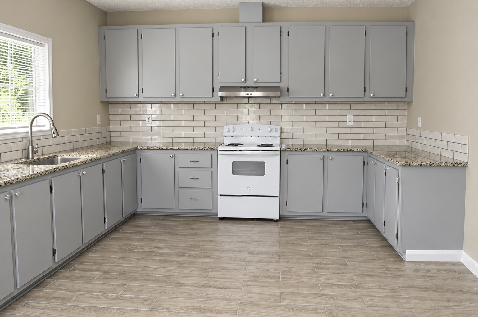 Spacious kitchen featuring elegant gray cabinetry, sleek granite countertops, and a classic white subway tile backsplash, complete with modern appliances and ample natural light.