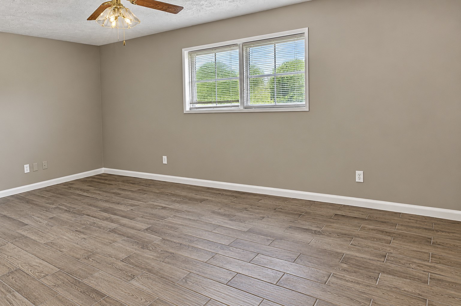 Spacious bedroom with wood-look tile flooring, neutral walls, and a ceiling fan, perfect for versatile living arrangements.