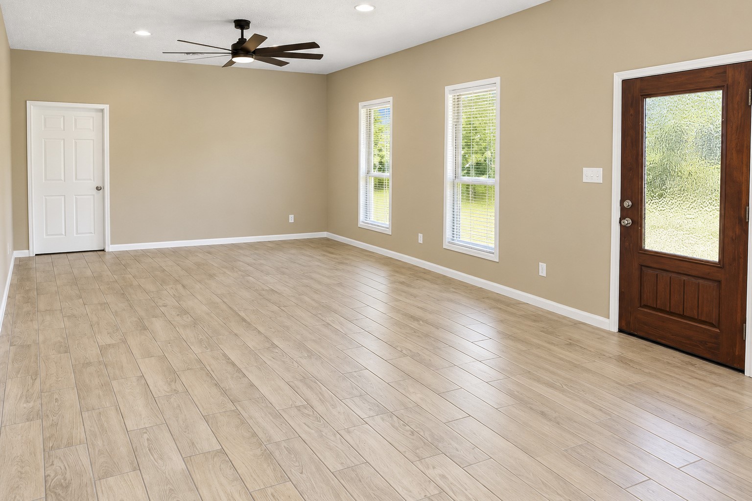 Spacious living area with elegant wood-style tile flooring, abundant natural light from large windows, and a stylish ceiling fan.
