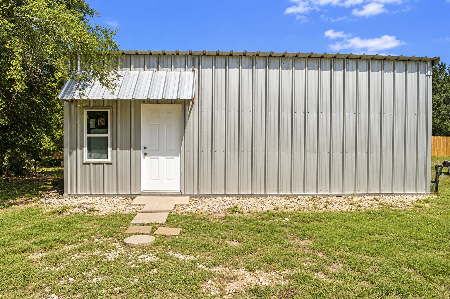 Charming metal-clad tiny multipurpose building with a welcoming entrance, nestled in a serene green setting.
