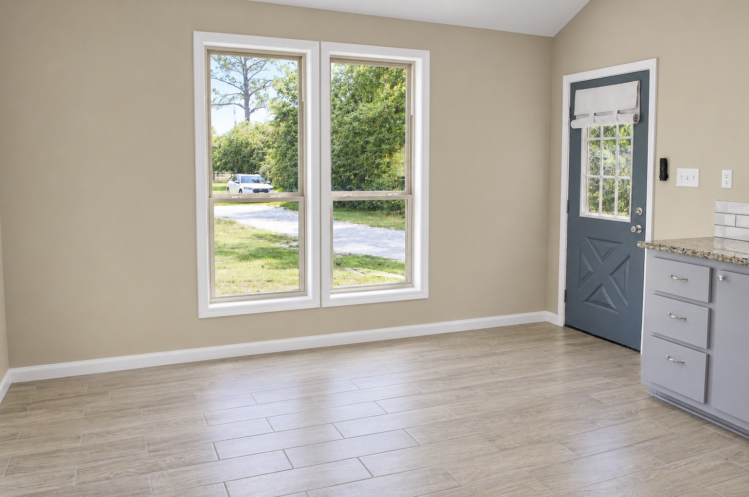 Bright and inviting breakfast space with large windows, wood-look tile flooring, and a charming blue door leading to the outside.