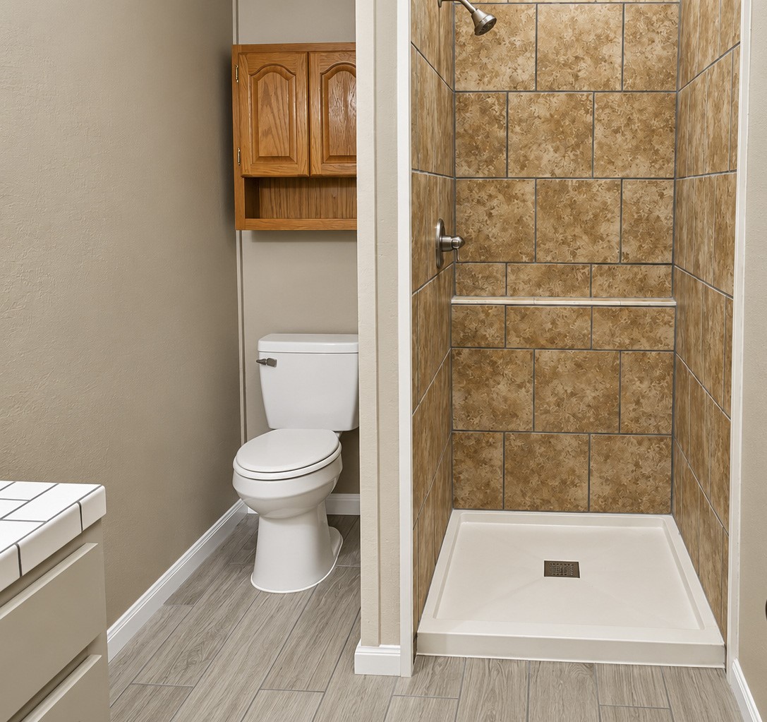 Bathroom with a tiled walk-in shower, sleek wood-look flooring, and a convenient storage cabinet above the toilet.