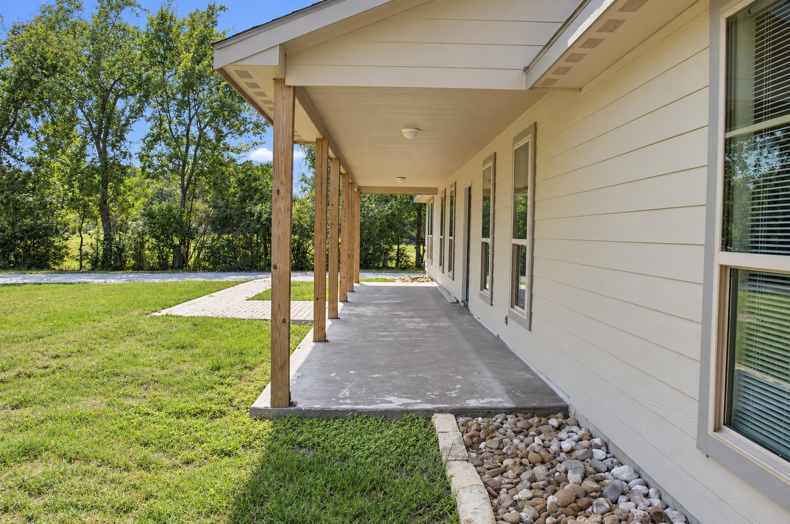 Charming covered porch with a concrete walkway and natural stone landscaping and a spacious yard.