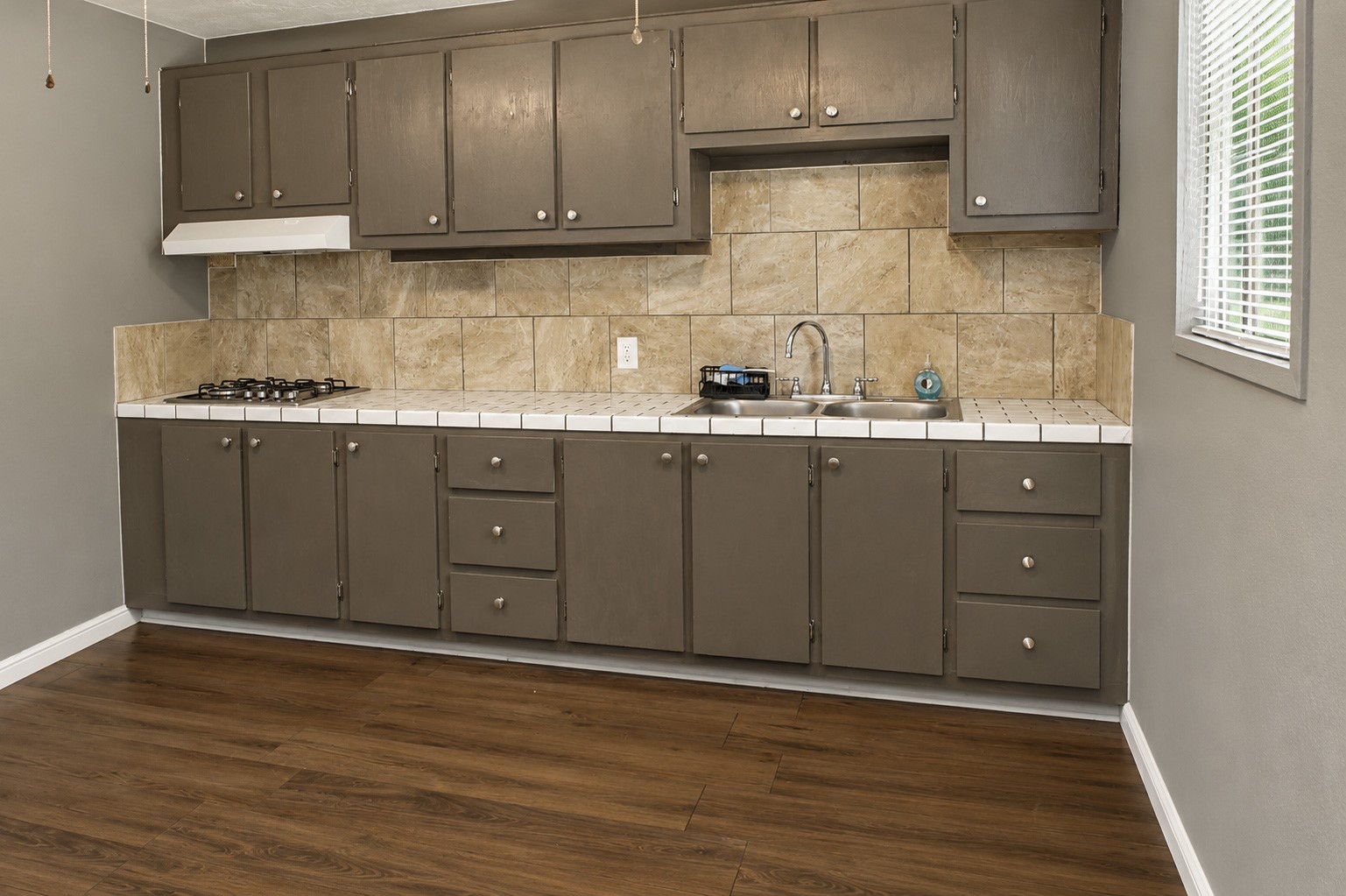 Quarter's kitchen with rustic brown cabinetry, sleek tile backsplash.