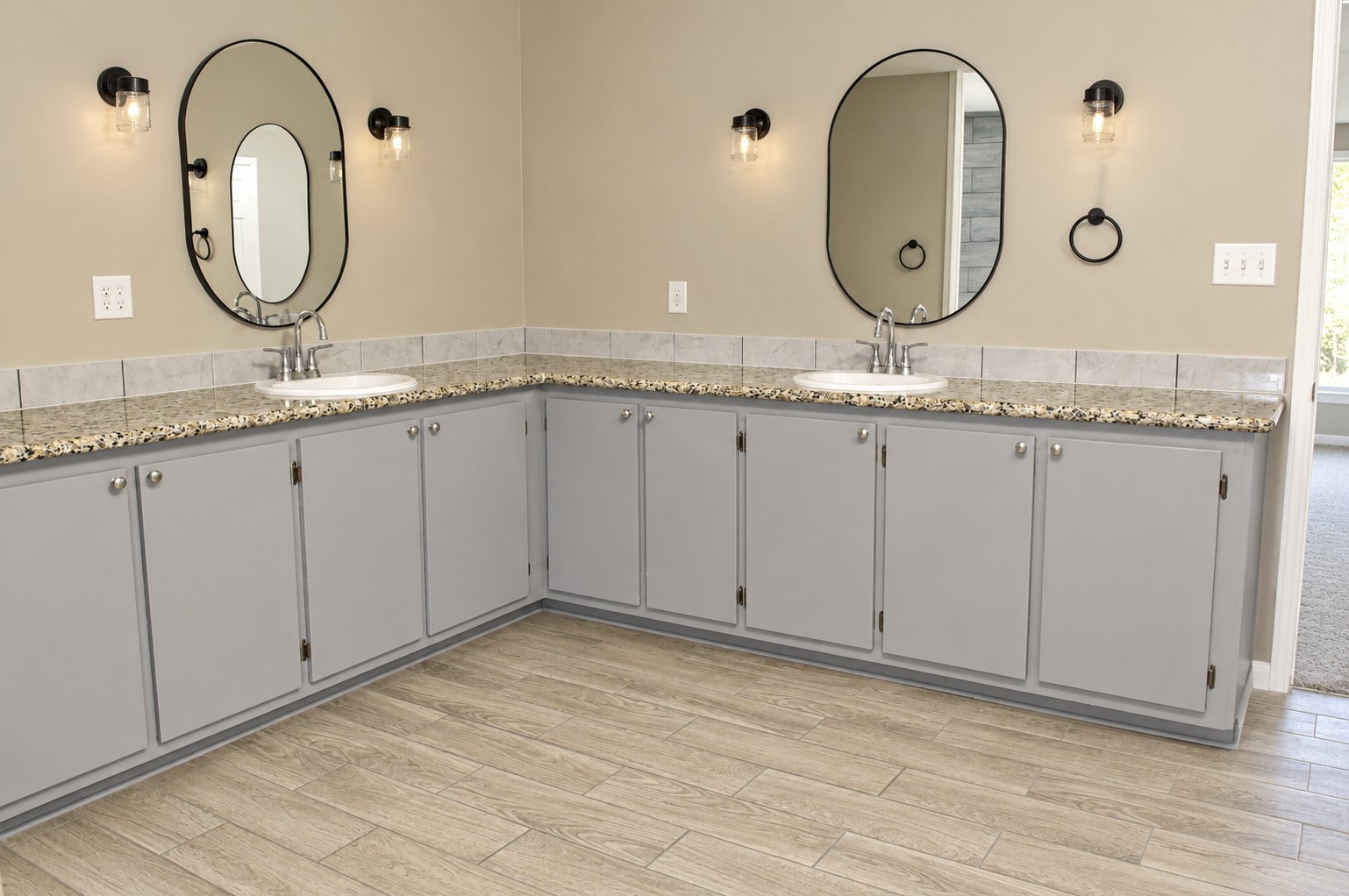 Spacious Primary bathroom featuring dual sinks with elegant granite countertops, sleek gray cabinetry, and stylish round mirrors enhanced by modern lighting.