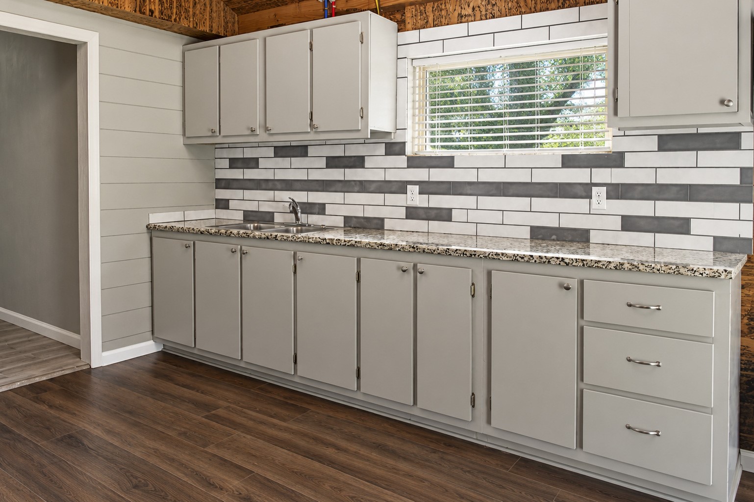 Additional kitchen on the split floor plan with sleek gray cabinetry, modern subway tile backsplash, and granite countertops, complemented by rich wood rustic walls.