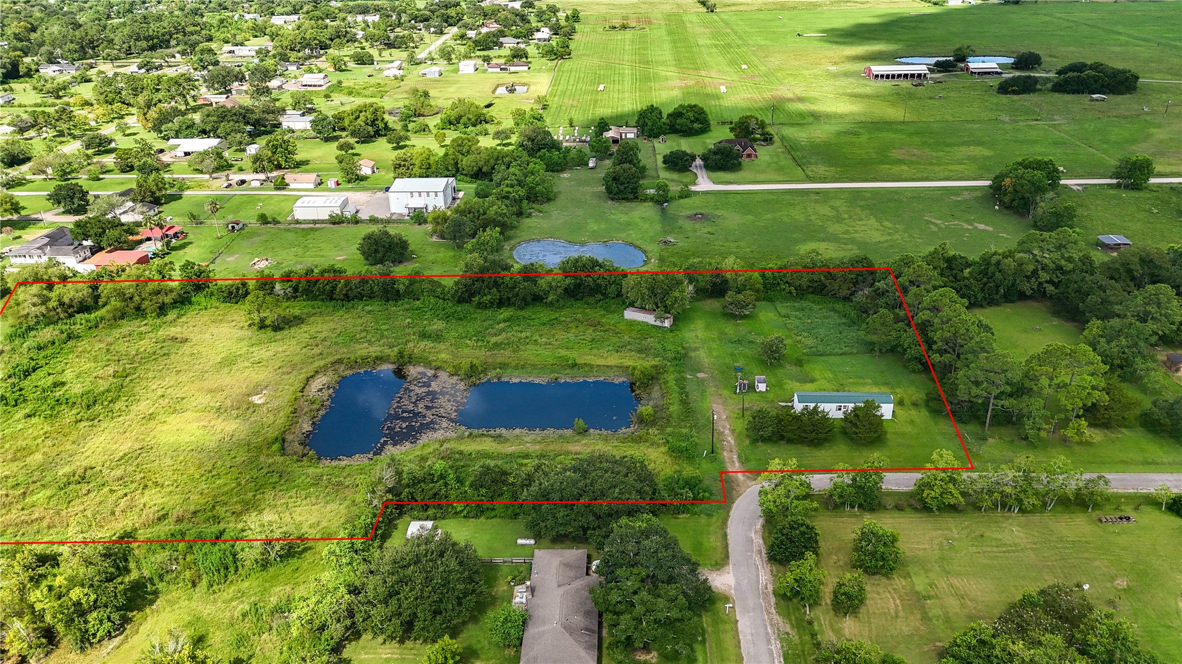 Expansive rural property with a serene pond, surrounded by lush greenery and open fields, offering peaceful seclusion and scenic views.
