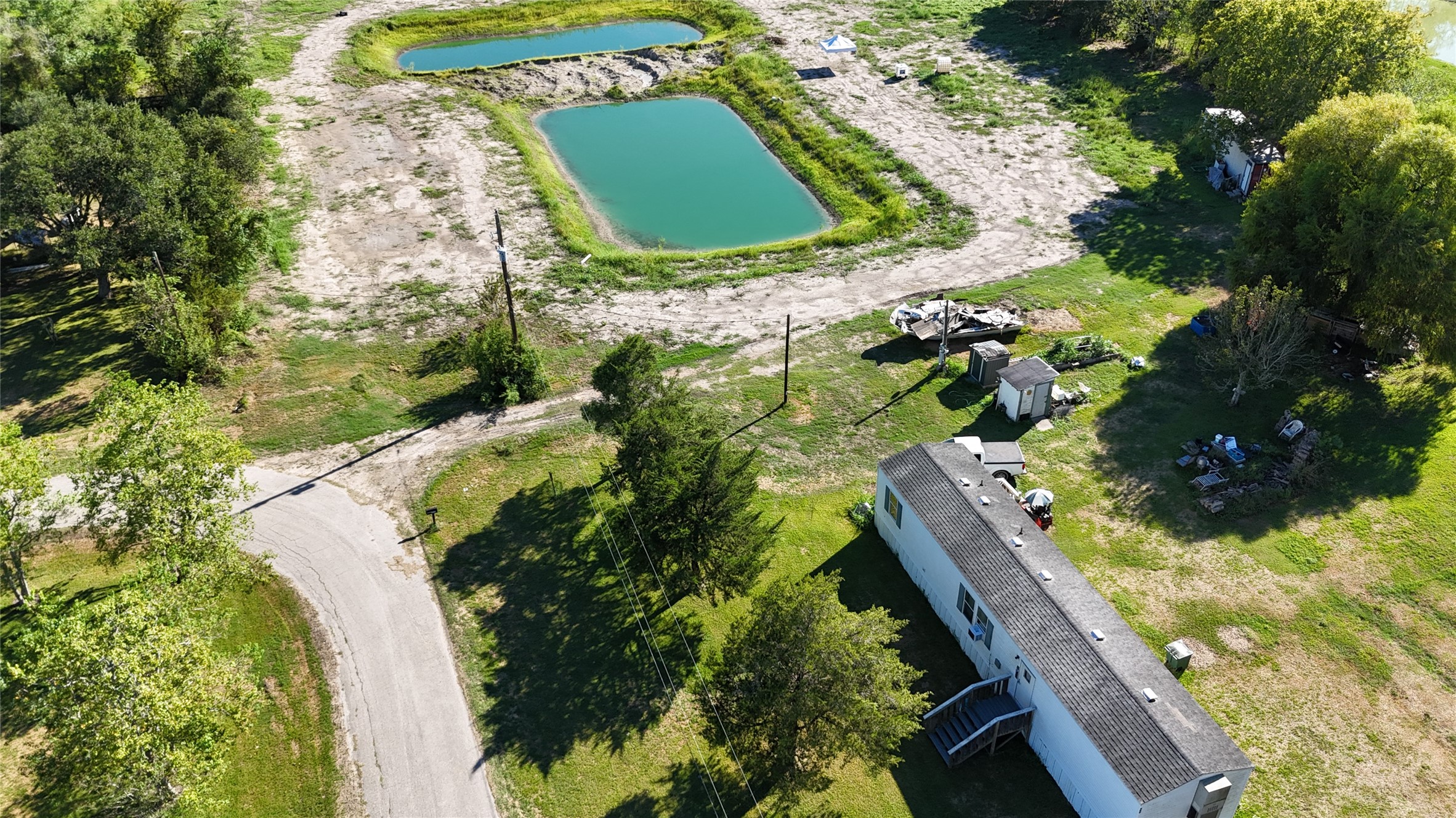 Expansive property with lush greenery, with a mobile home, and a serene pond, offering a tranquil rural escape.