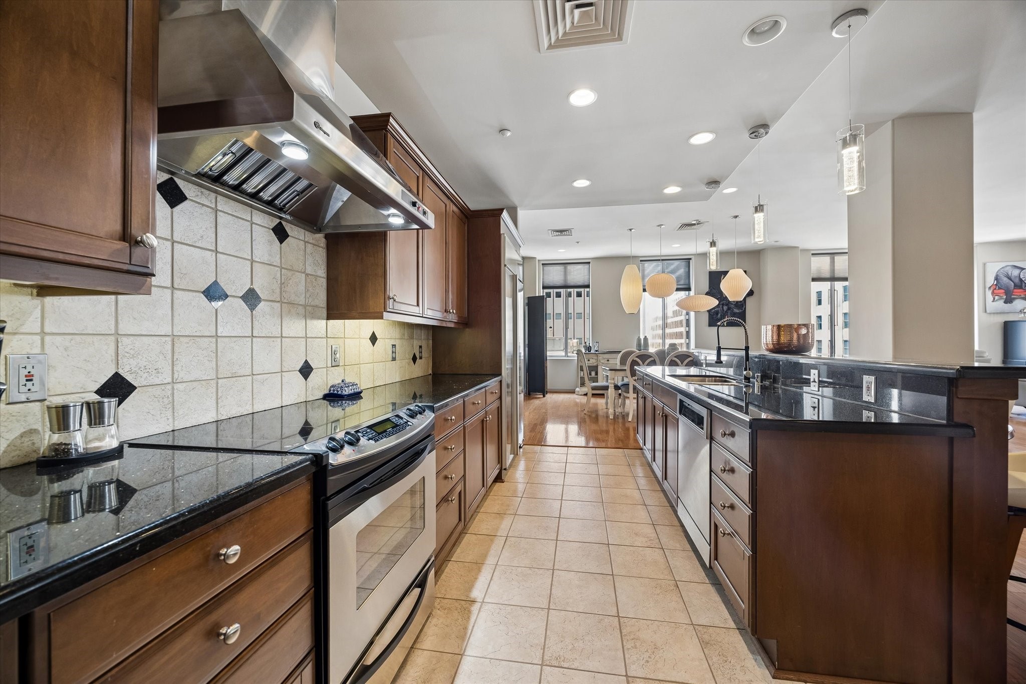 Elegant kitchen featuring rich wood cabinetry, sleek granite countertops, and modern stainless steel appliances, seamlessly flowing into a bright, open living space.
