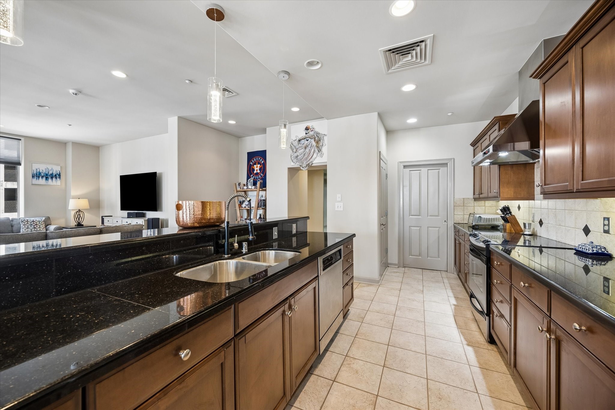 Spacious, modern kitchen with sleek black countertops, rich wooden cabinets, and stainless steel appliances, seamlessly connected to an inviting living area.