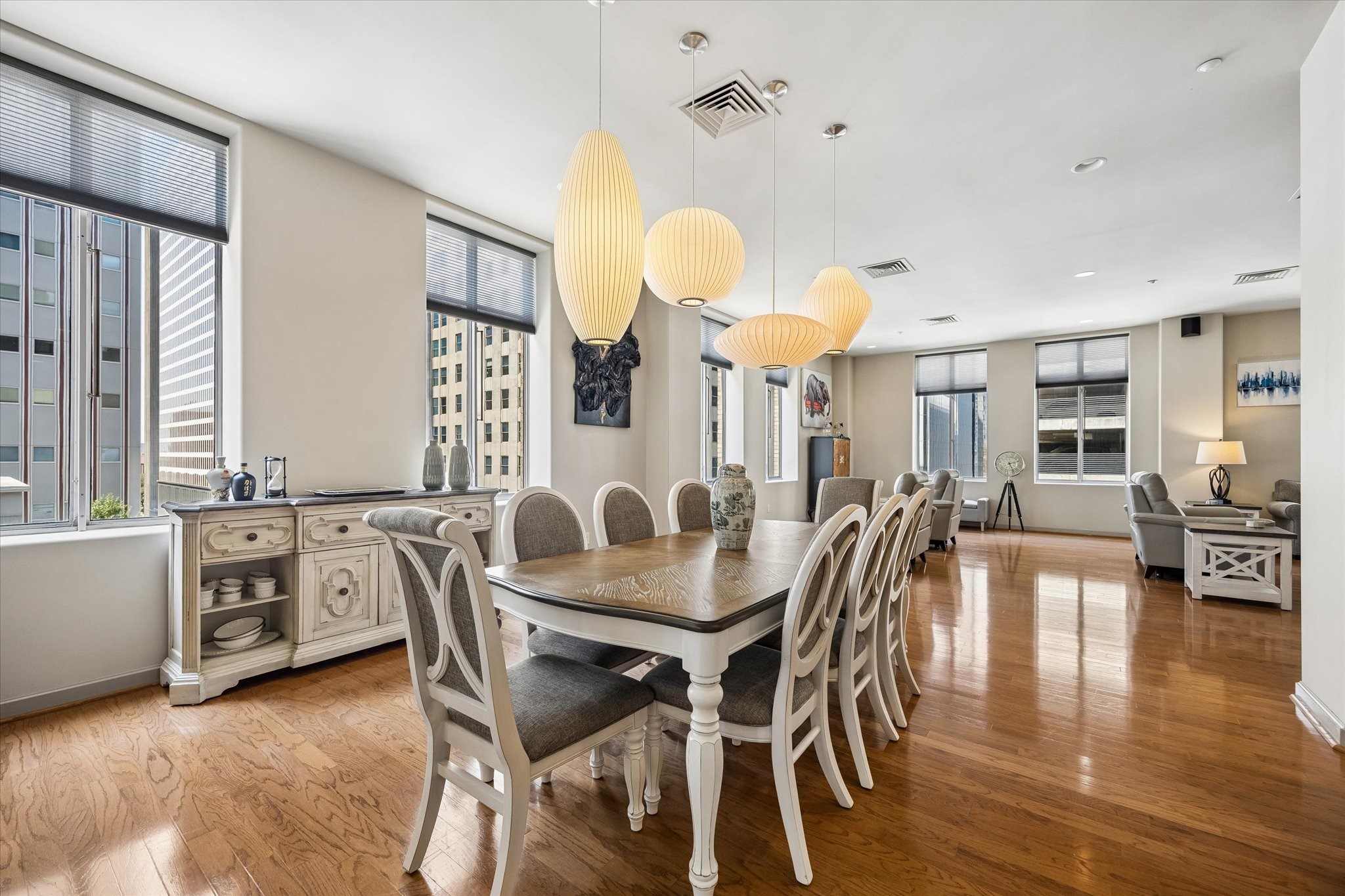 Spacious dining area with elegant lighting and large windows offering city views, seamlessly flowing into a cozy living space with modern decor. Spacious dining area with elegant lighting and large windows offering city views, seamlessly flowing into a cozy living space with modern decor.