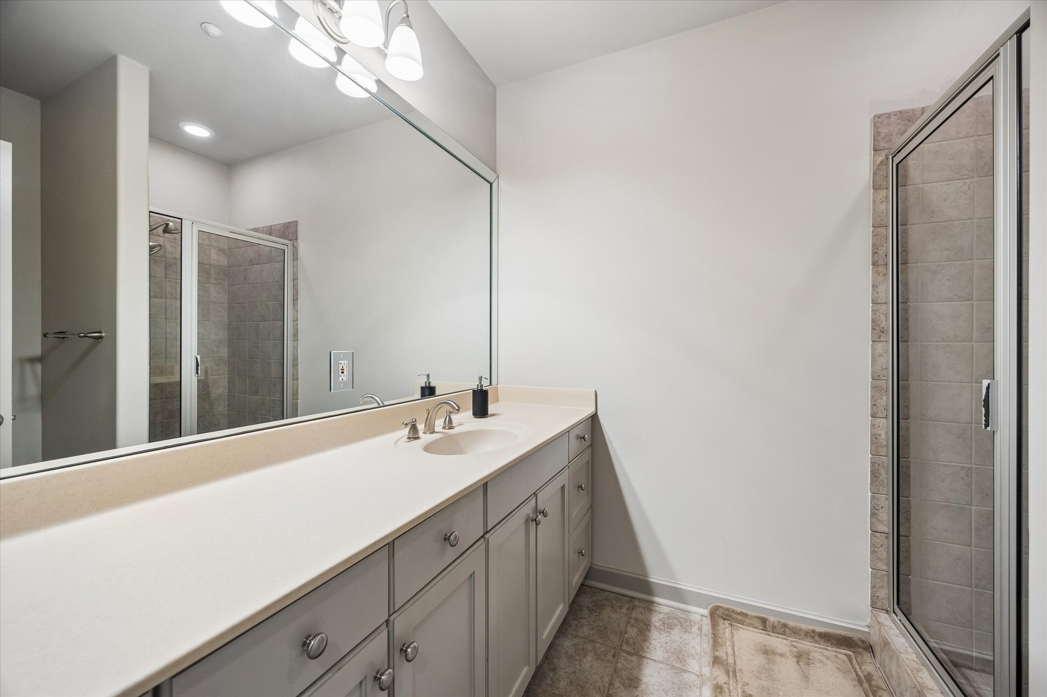 Spacious bathroom featuring a large vanity with ample storage, elegant fixtures, and a sleek, glass-enclosed shower.