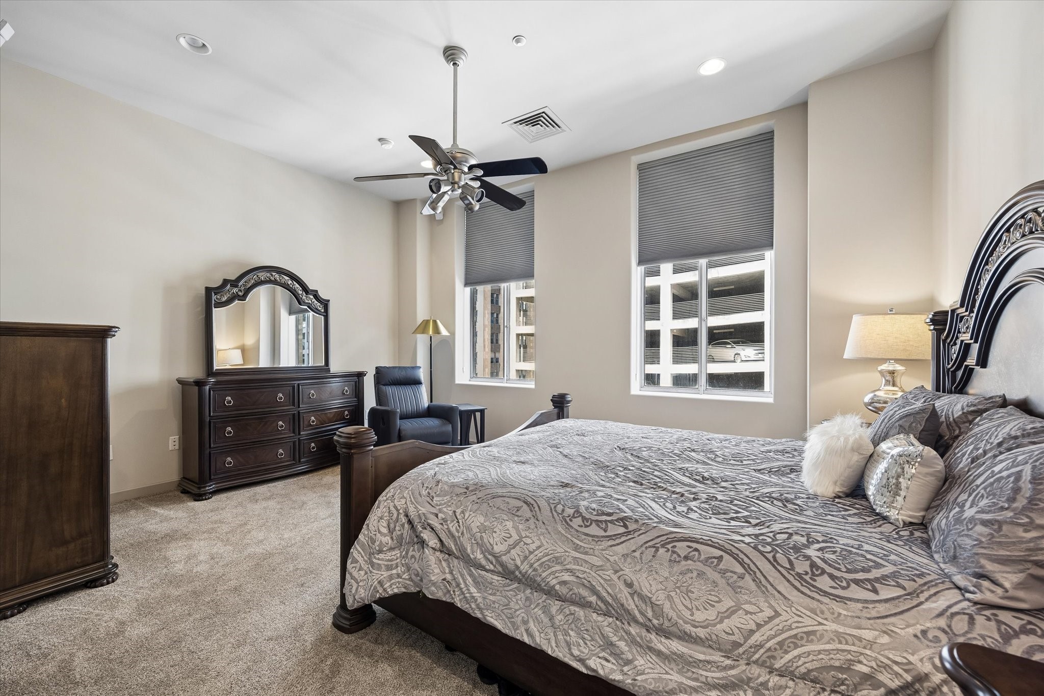 Spacious primary bedroom featuring elegant dark wood furniture, plush carpeting, and ample natural light from large windows.
