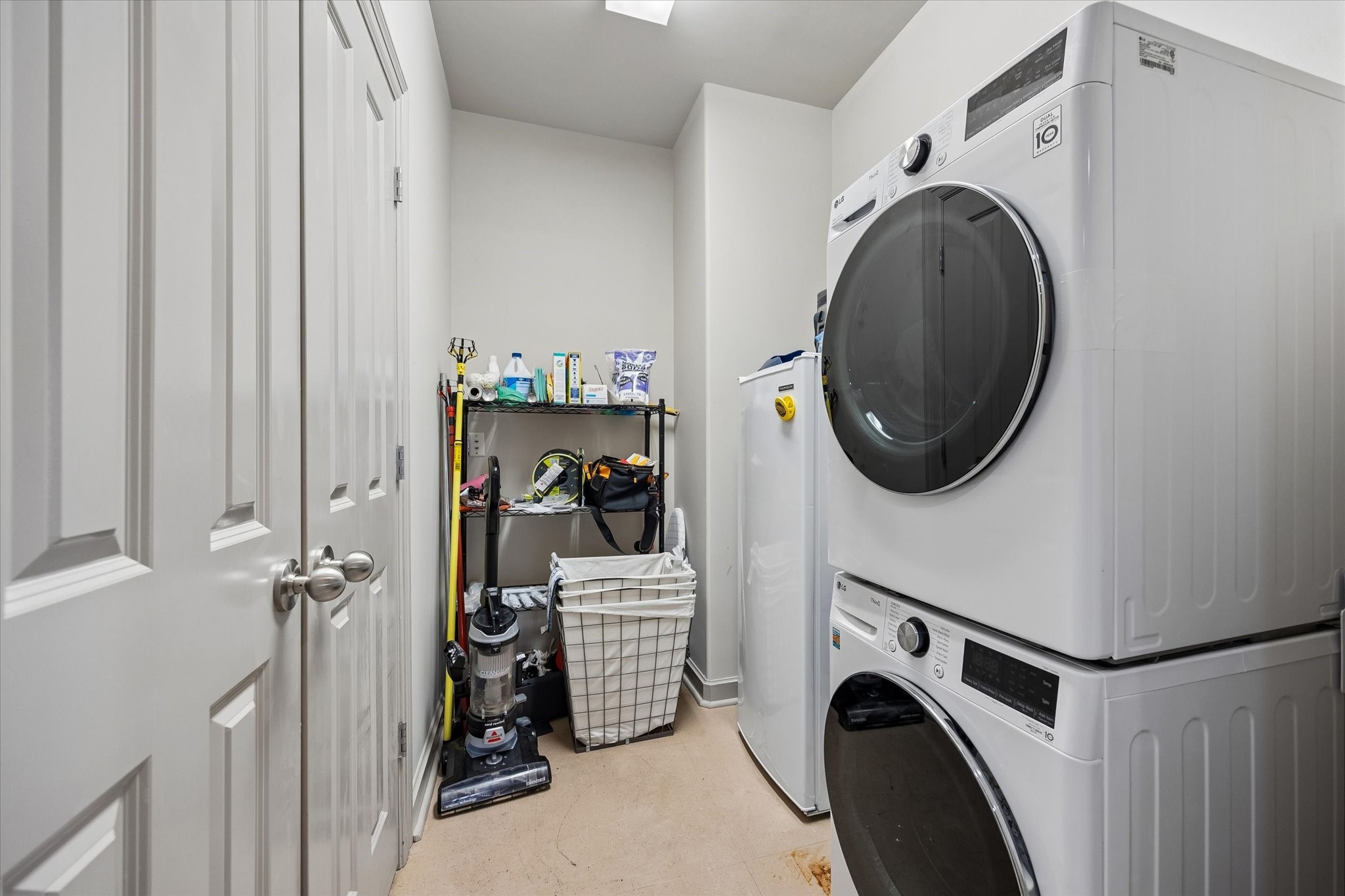Efficient laundry room with stackable washer and dryer, ample shelving for storage, and additional space for cleaning supplies.