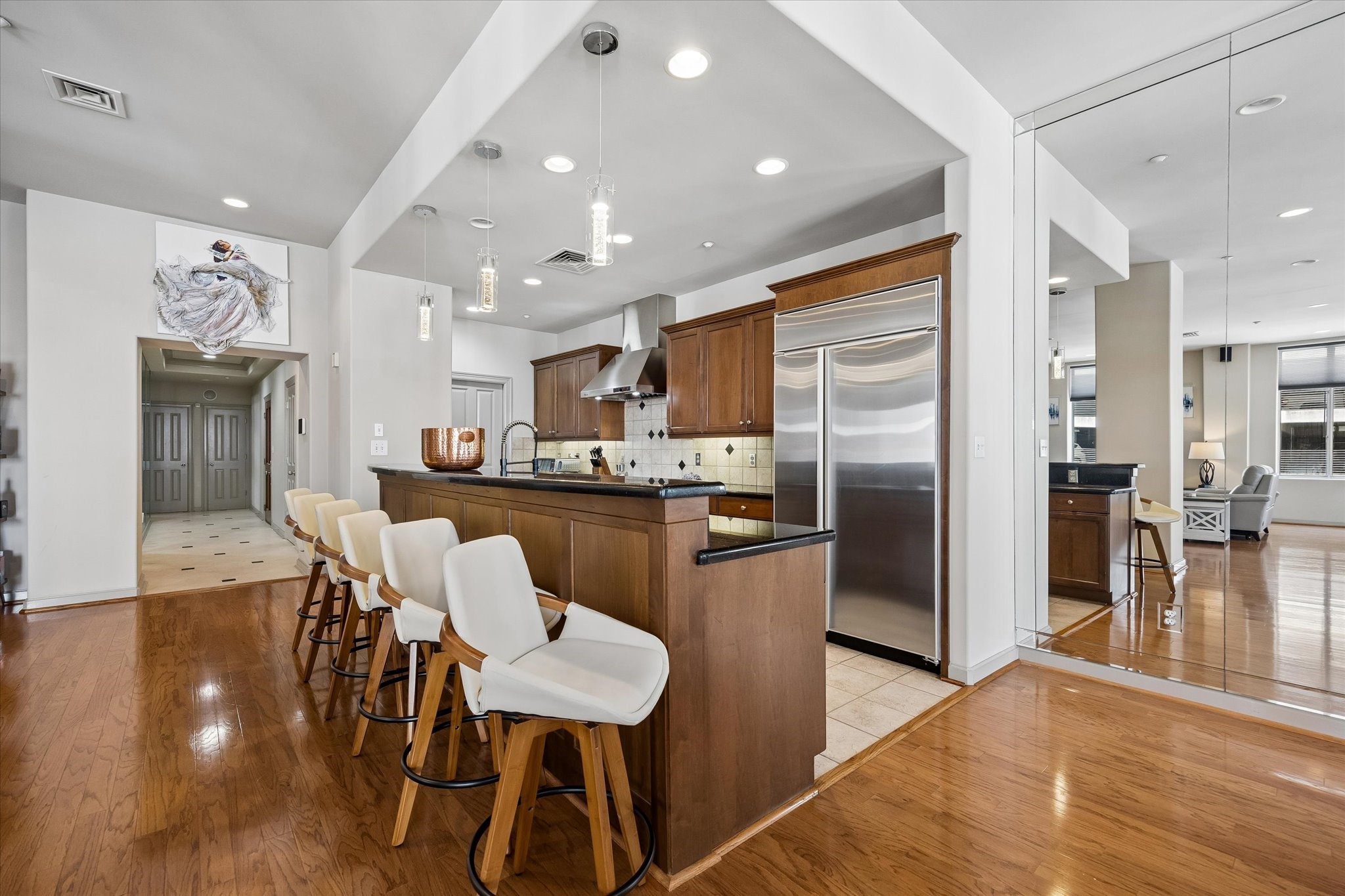 Spacious kitchen with sleek stainless steel appliances, elegant dark countertops, and a large breakfast bar with stylish seating, seamlessly flowing into an inviting open-concept living area.