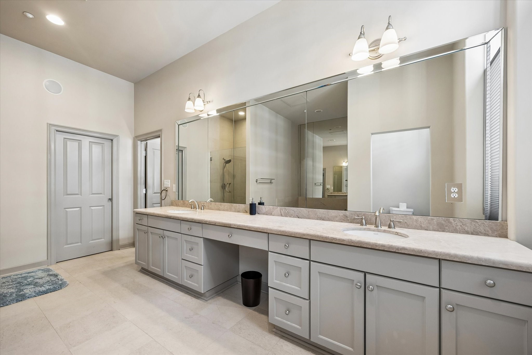 Spacious bathroom featuring a long double vanity with ample storage, a large mirror, and elegant lighting, complemented by a sleek walk-in shower.