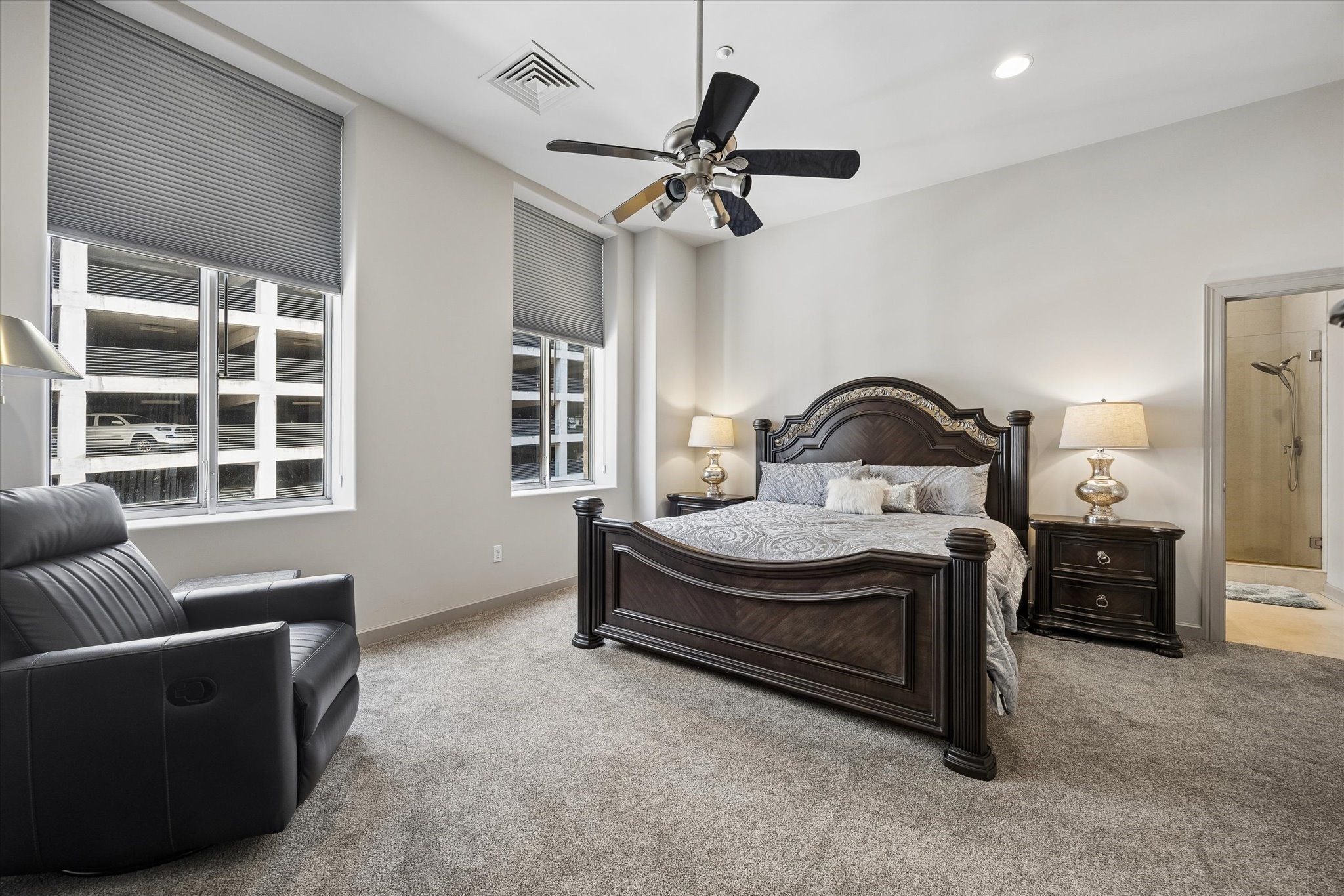 Spacious Primary bedroom featuring elegant dark wood furniture, plush carpeting, and ample natural light from large windows, complemented by a cozy seating area and en-suite bathroom access.