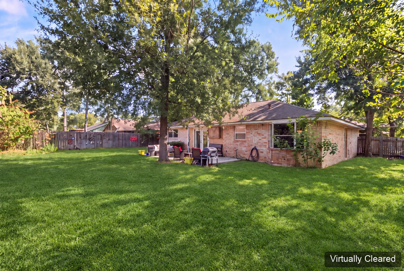 Virtually cleared rear-yard perspective showing the home's brick exterior and tree canopy. The original photo at the end shows existing yard features.