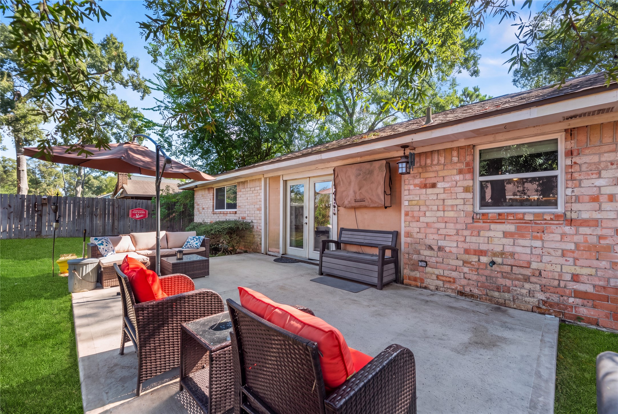 Back patio beside the brick rear exterior, with space for outdoor seating beneath the trees.