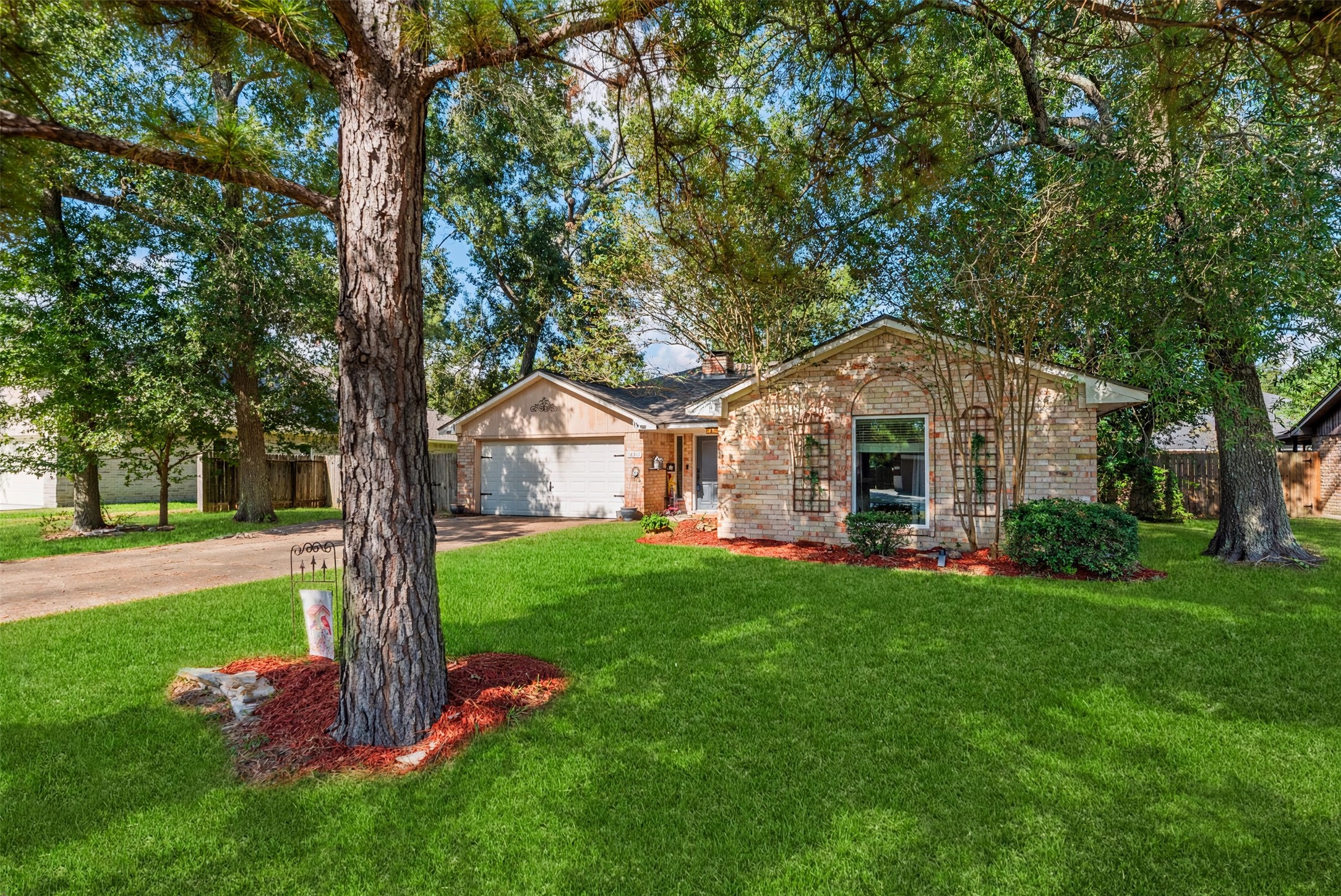 16511 Port O Call Street: a brick home framed by mature trees, with a broad front lawn and a driveway leading to the garage.
