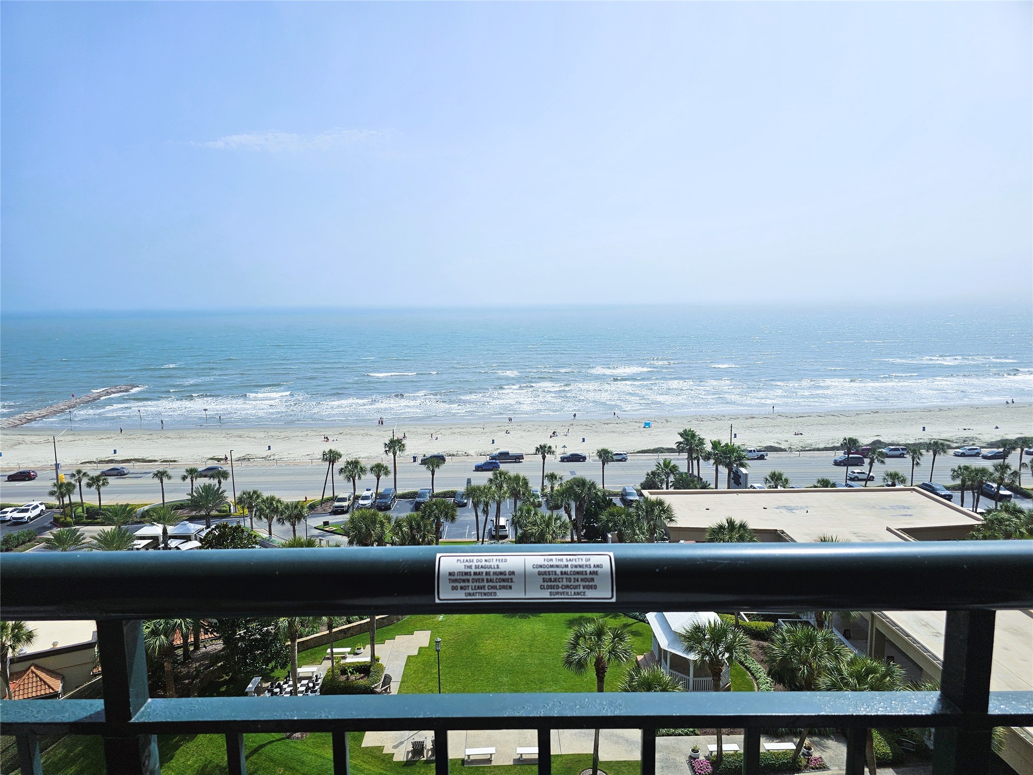 Stunning oceanfront view from a spacious balcony, overlooking a sandy beach and sparkling blue waters, perfect for seaside relaxation.