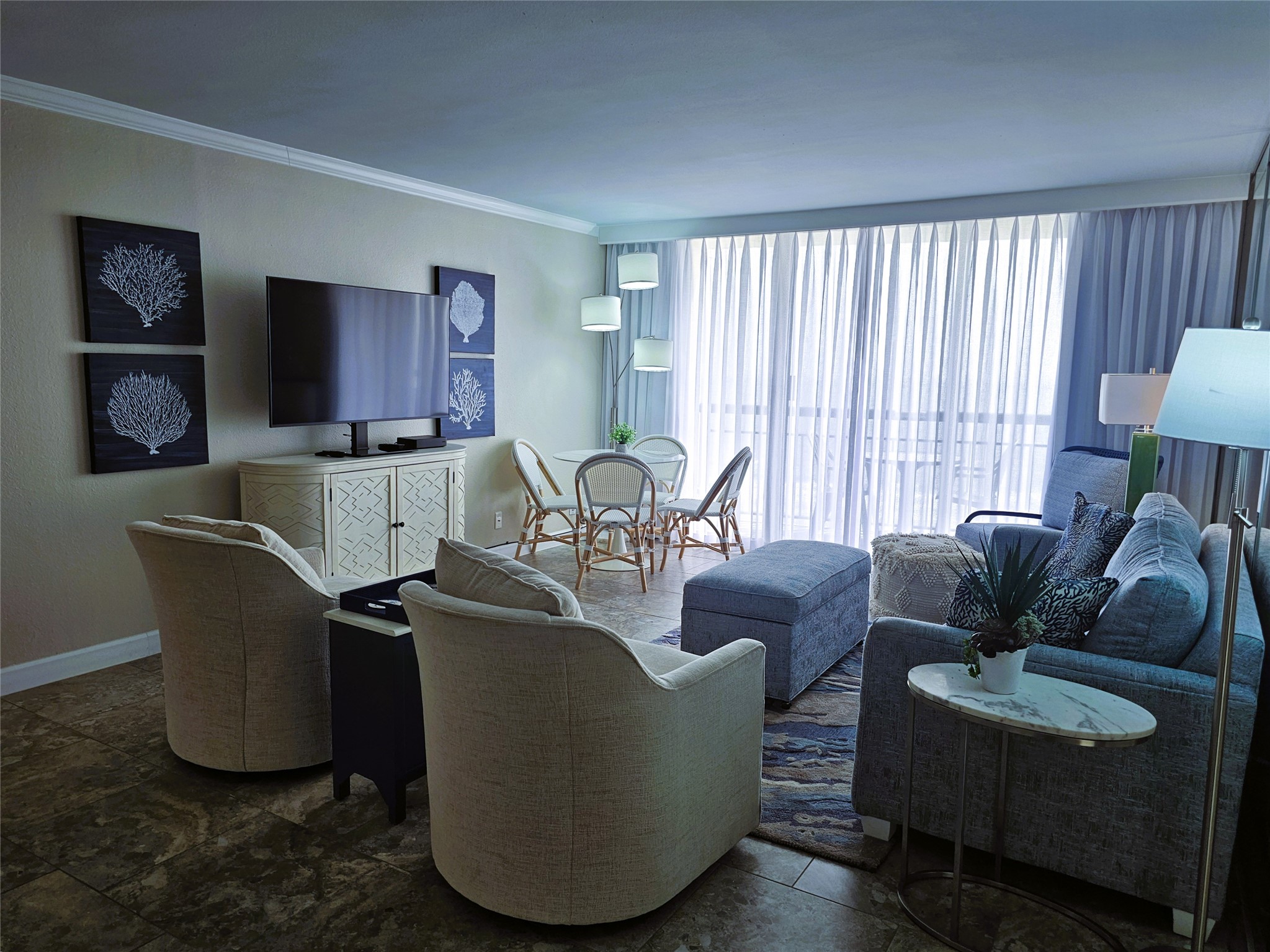 Bright and inviting living space with modern furnishings, a large flat-screen TV, and elegant decor. Floor-to-ceiling windows allow natural light to fill the room, creating a warm and welcoming atmosphere.