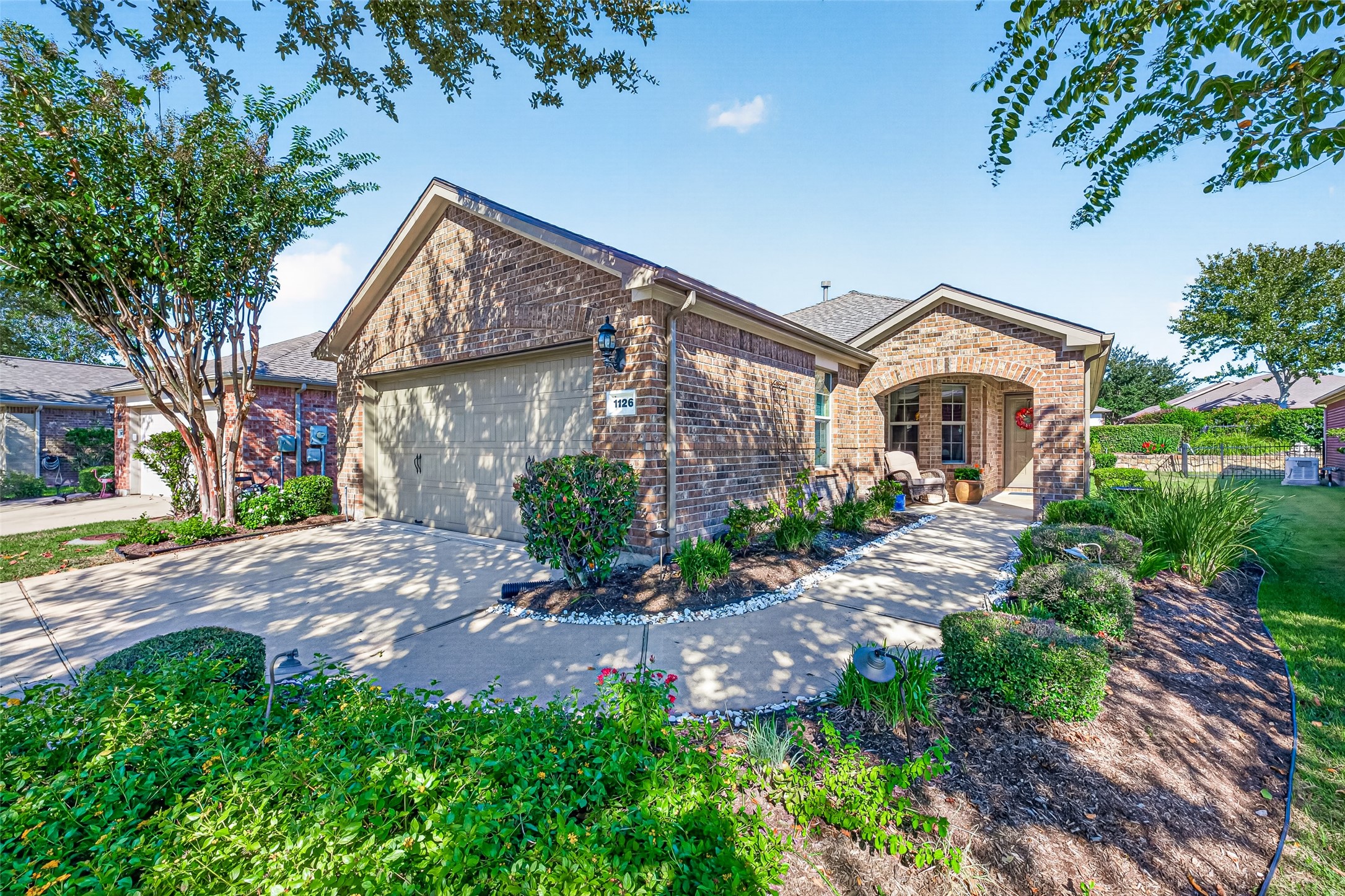 Welcoming brick exterior framed by mature trees and colorful landscaping.