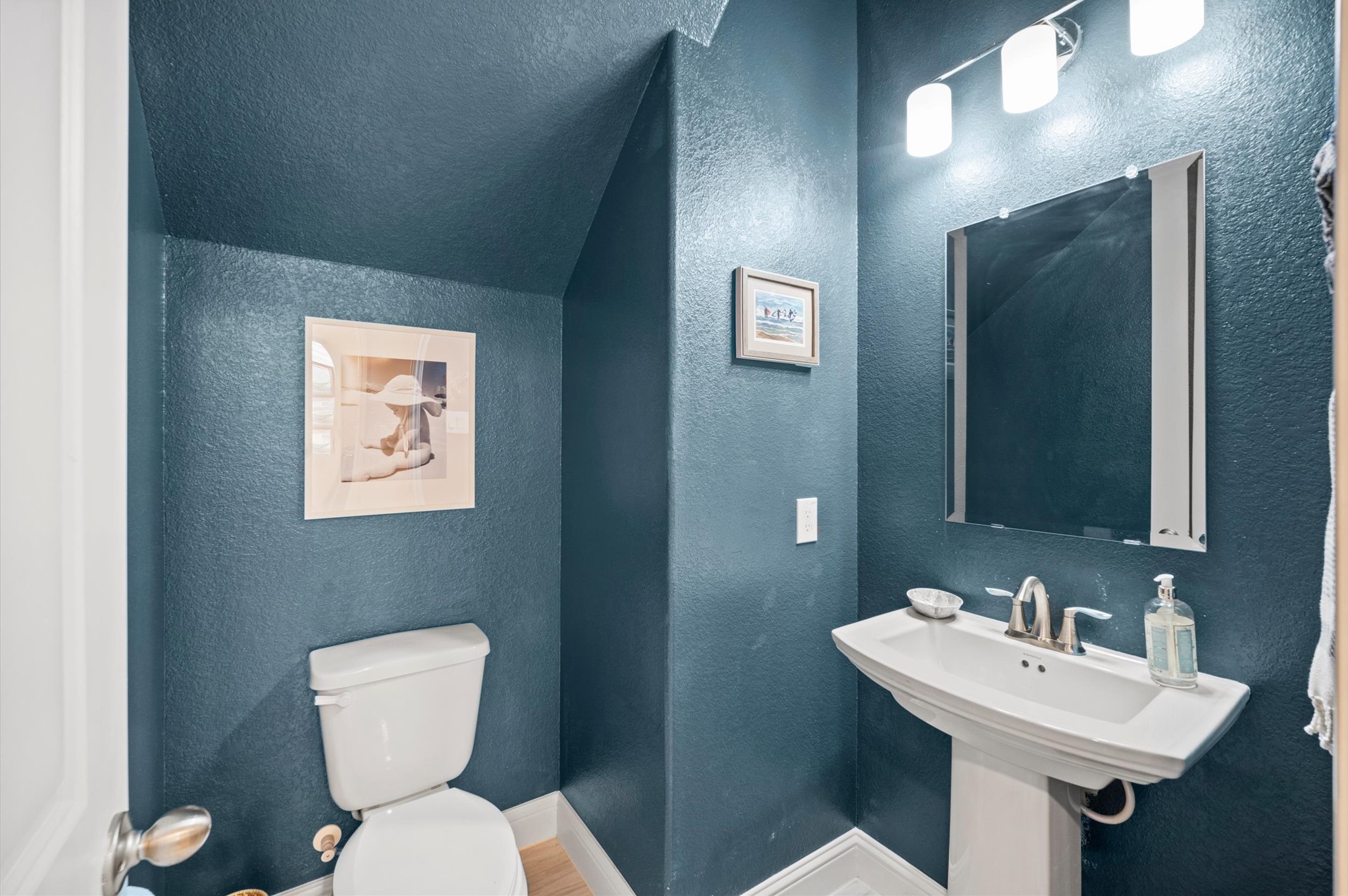 Charming powder room with elegant navy walls, a sleek pedestal sink, and modern lighting.