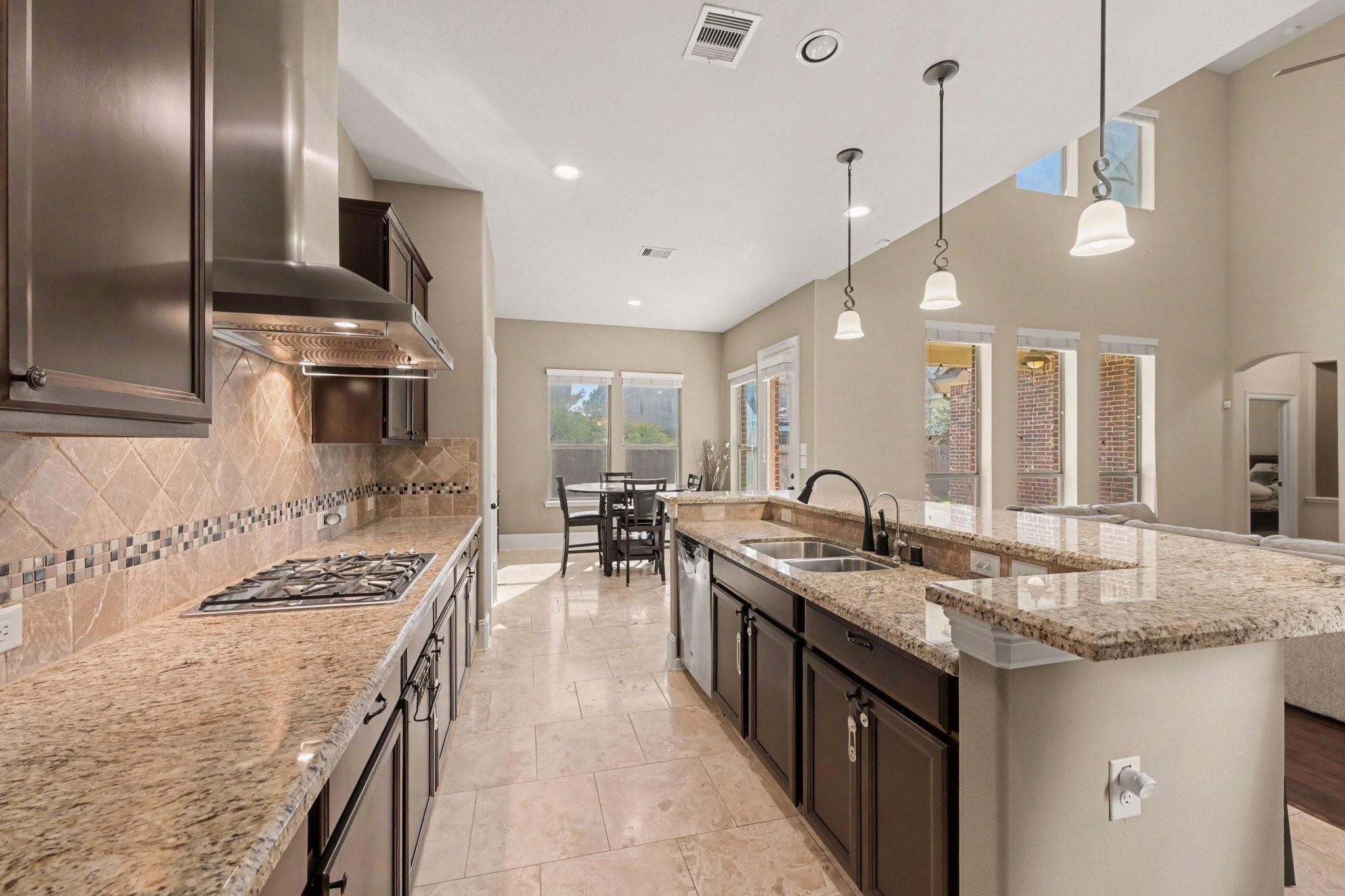 Spacious open-concept kitchen featuring granite countertops, rich wood cabinetry, stainless steel appliances, a gas cooktop, and a generous breakfast bar.