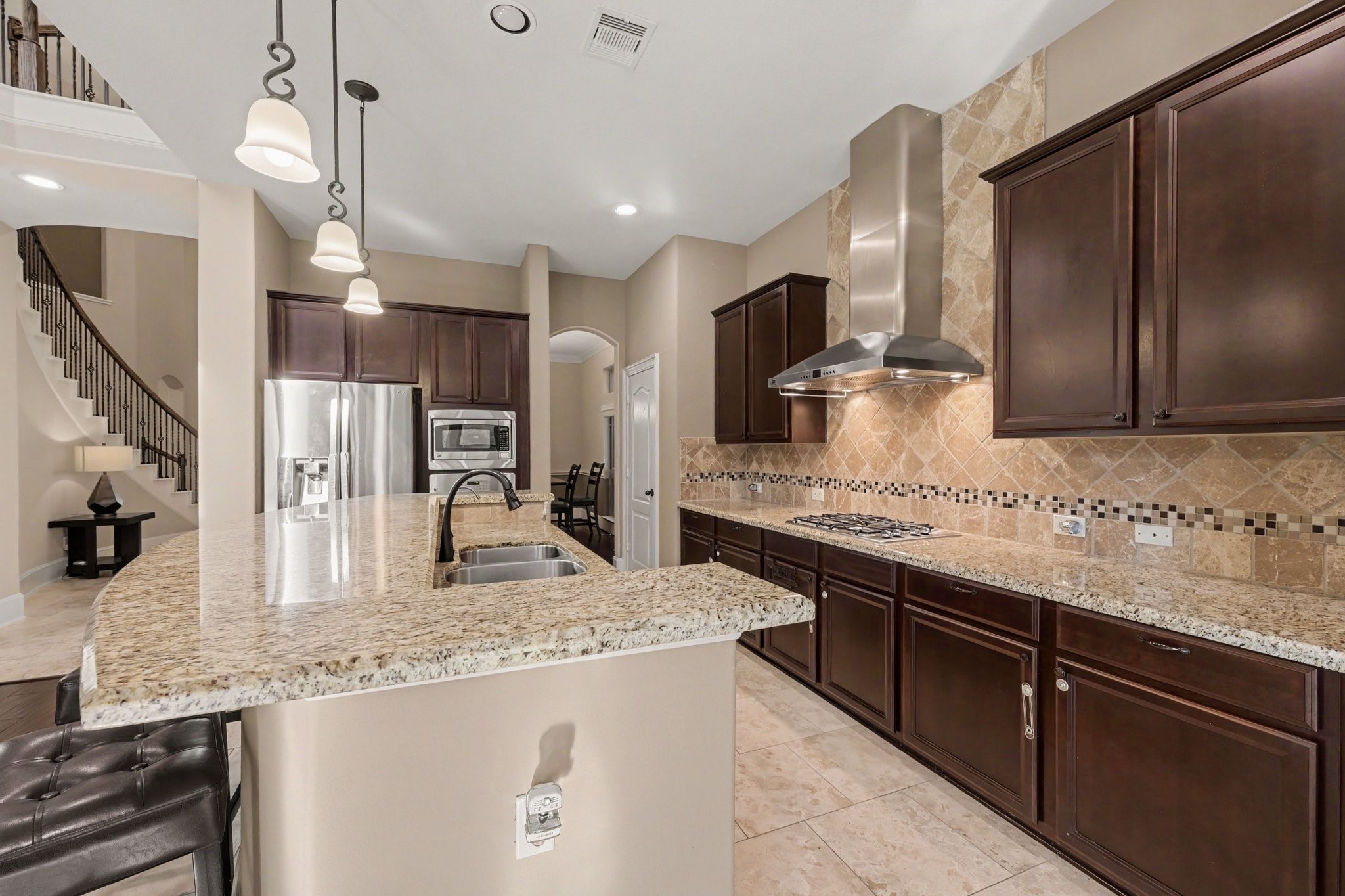 Spacious open-concept kitchen featuring granite countertops, rich wood cabinetry, stainless steel appliances, a gas cooktop, and a generous breakfast bar.