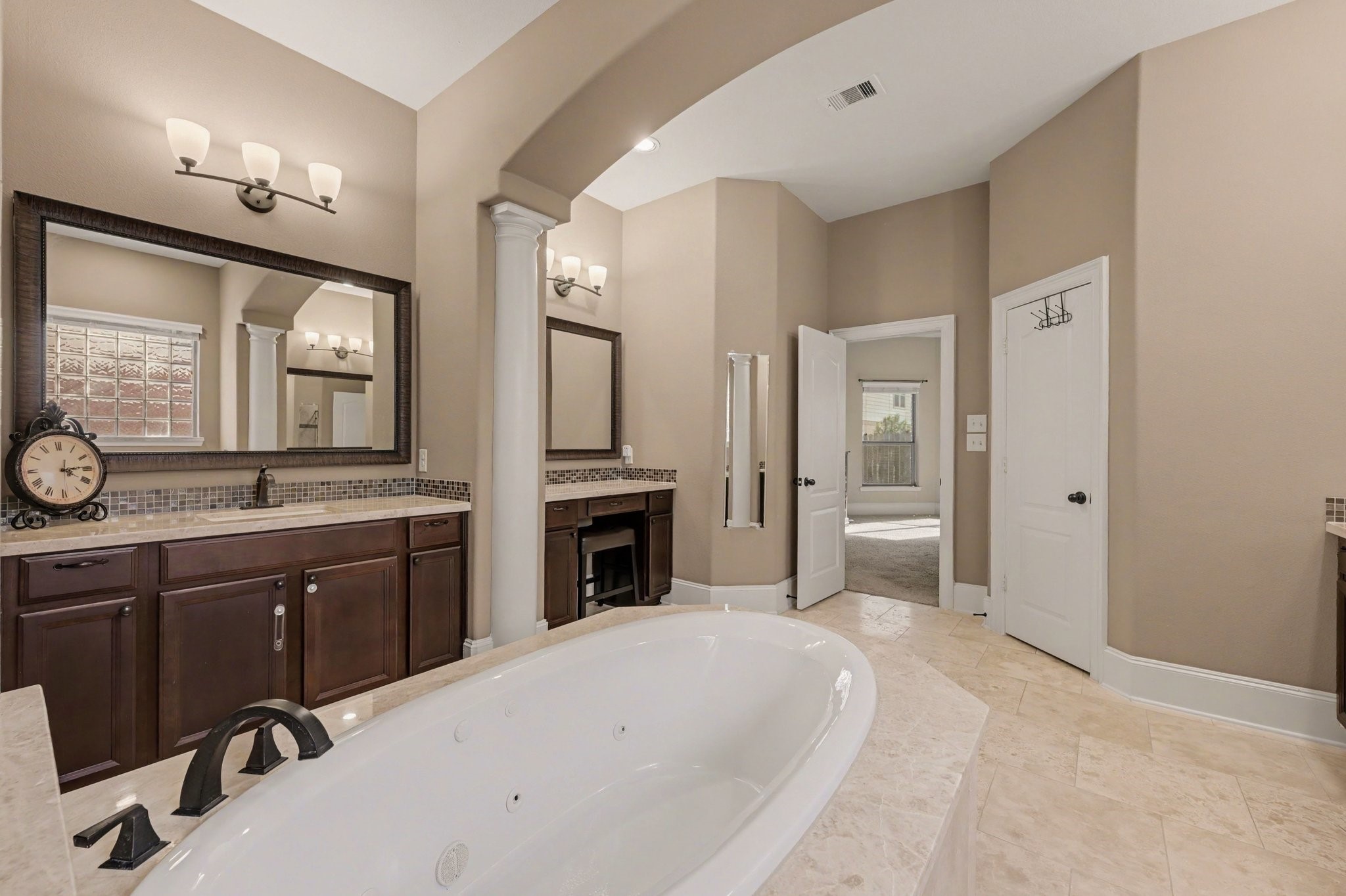 Another view of the primary bathroom, highlighting the elegant architectural details, generous vanity space, and access to two separate walk-in closets.