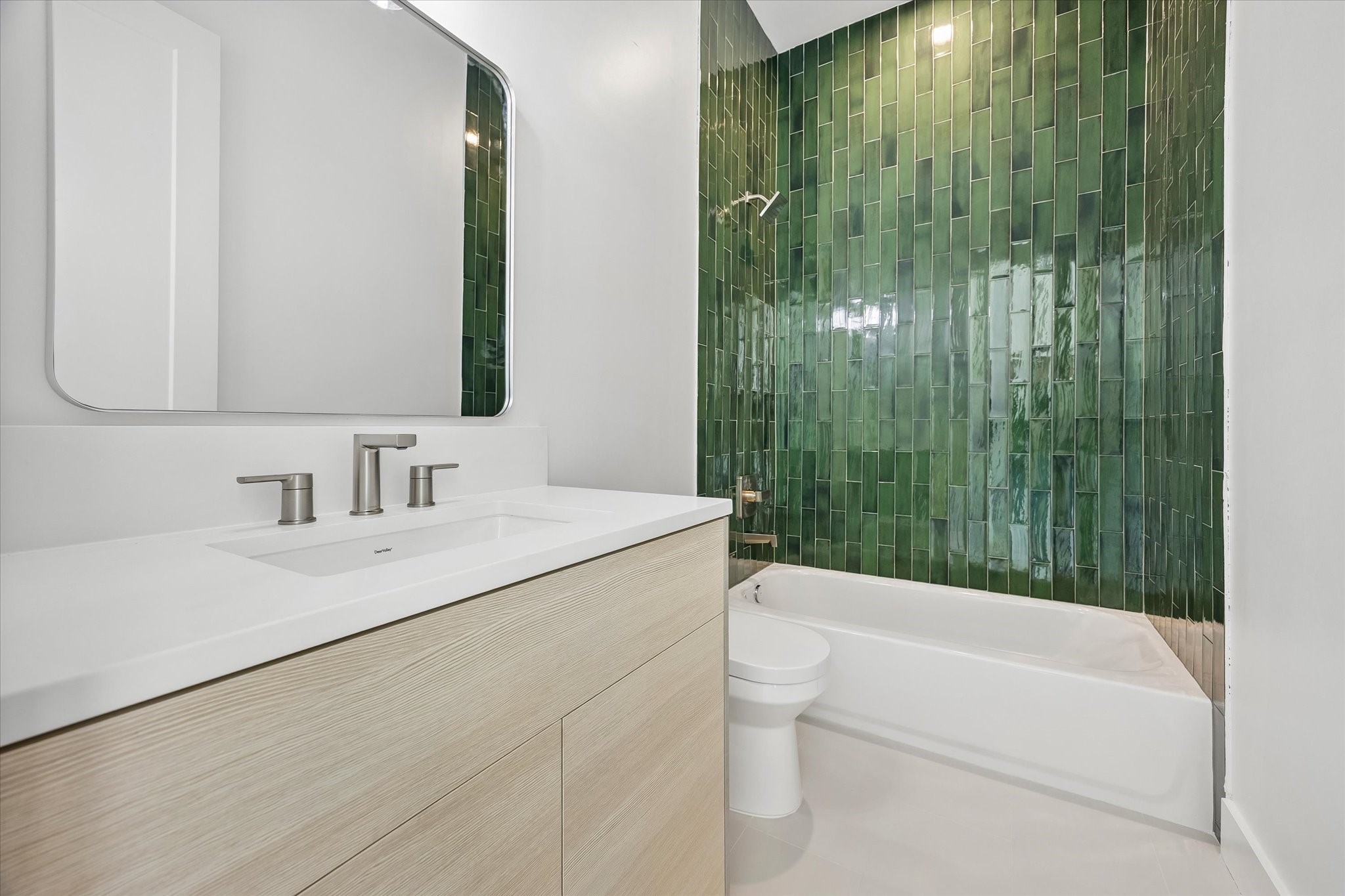 Private en-suite bathroom for the second-floor secondary bedroom features a light wood-toned vanity w/ quartz countertop, integrated sink & storage below. Tub/shower combination features decorative tile surround and built-in soap niche. Conveniently located adjacent to the bedroom's walk-in closet.