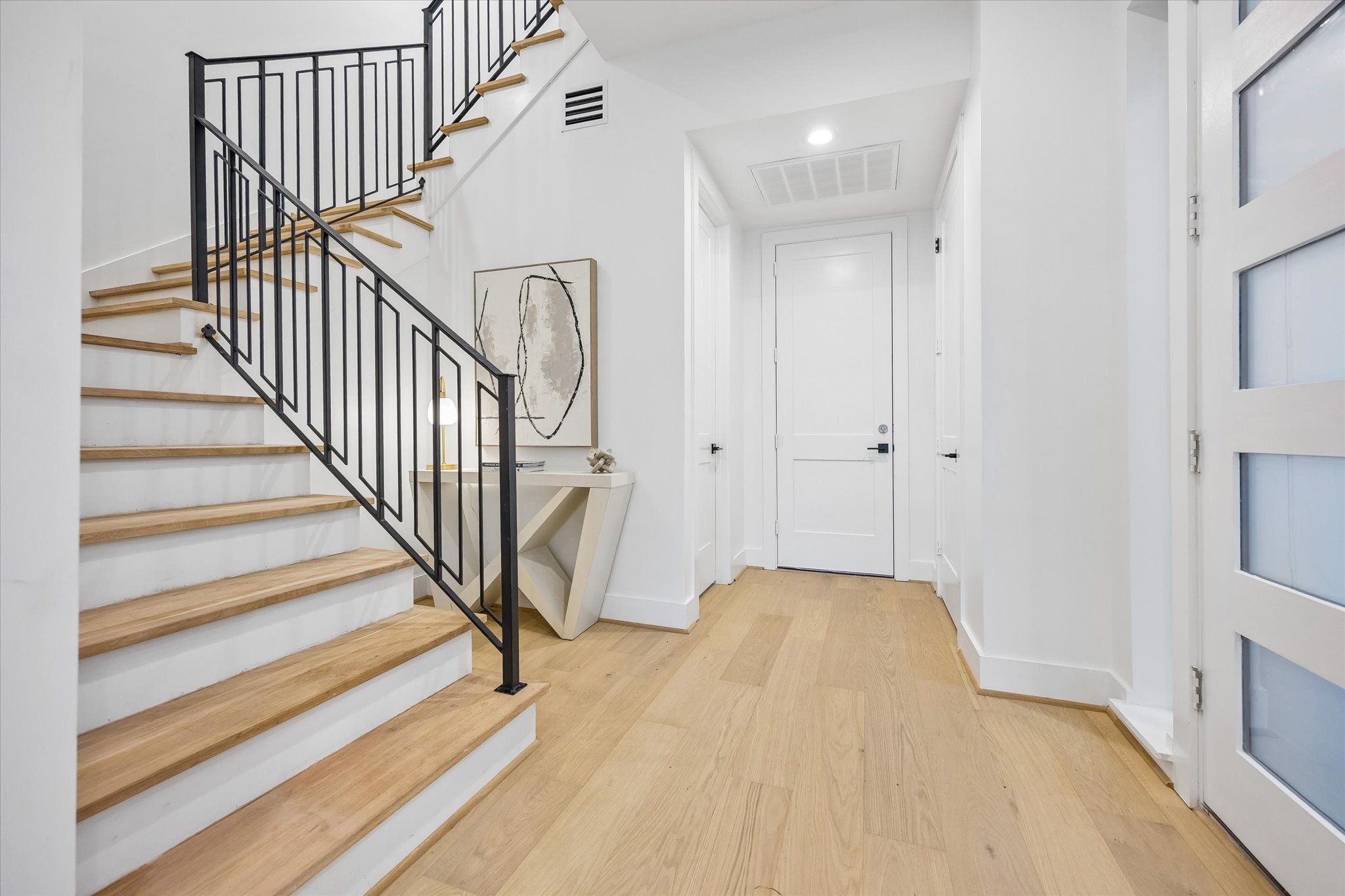 Another look at the beautiful entry highlighting the decorative staircase w/ modern black metal railing. Elevator-capable closet (to the right) are thoughtfully positioned on all 3 floors for future elevator installation. Entry provides convenient access to the powder bath (on the left), attached garage (straight ahead) & open-concept living areas.