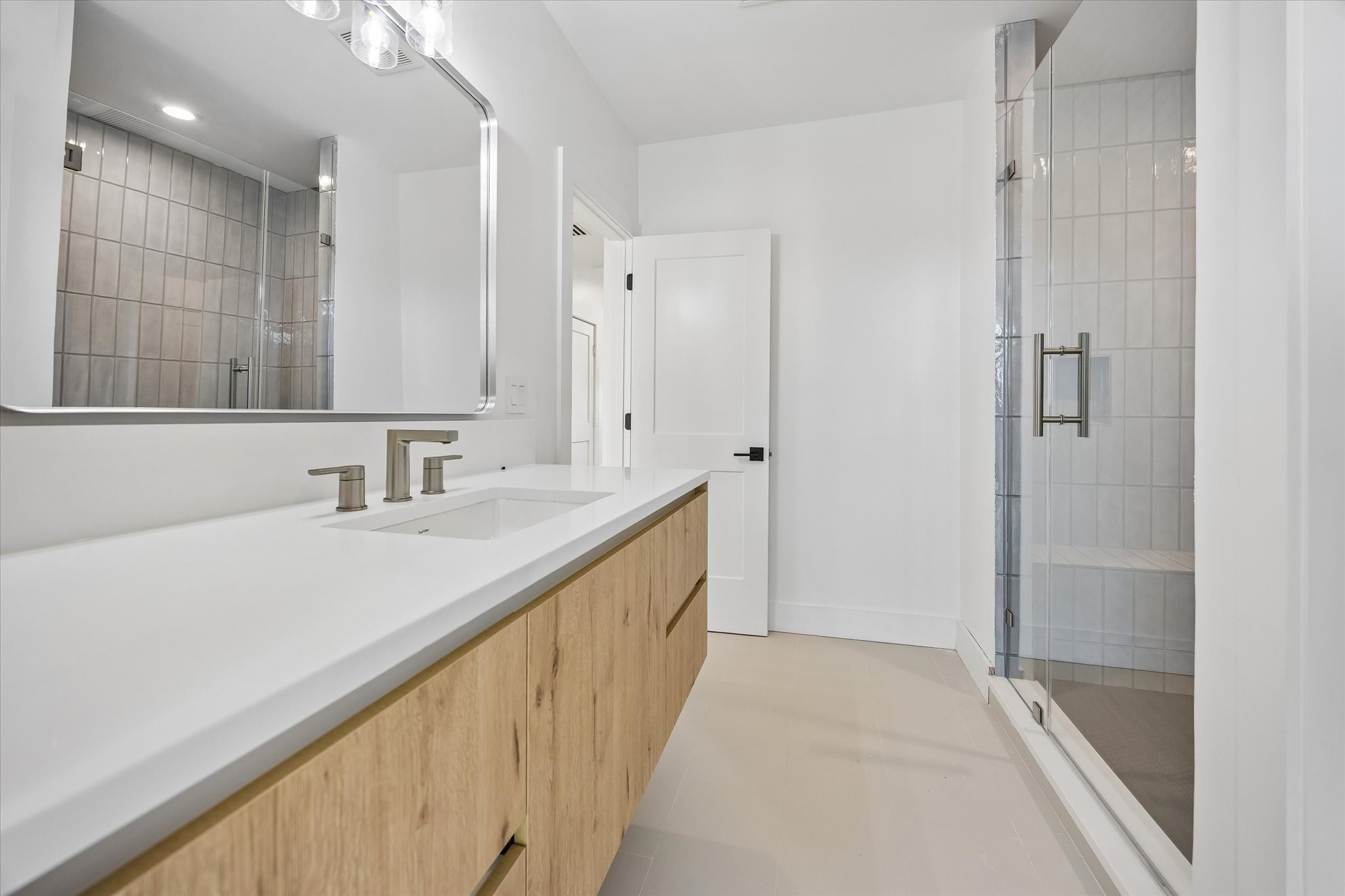 Beautiful third-floor secondary bathroom features quartz countertops, wood-toned vanity w/ storage & walk-in shower with frameless glass door, decorative tile surround & built-in soap niche. Private water closet adds convenience. Accessible from both the third-floor hallway and secondary bedroom.