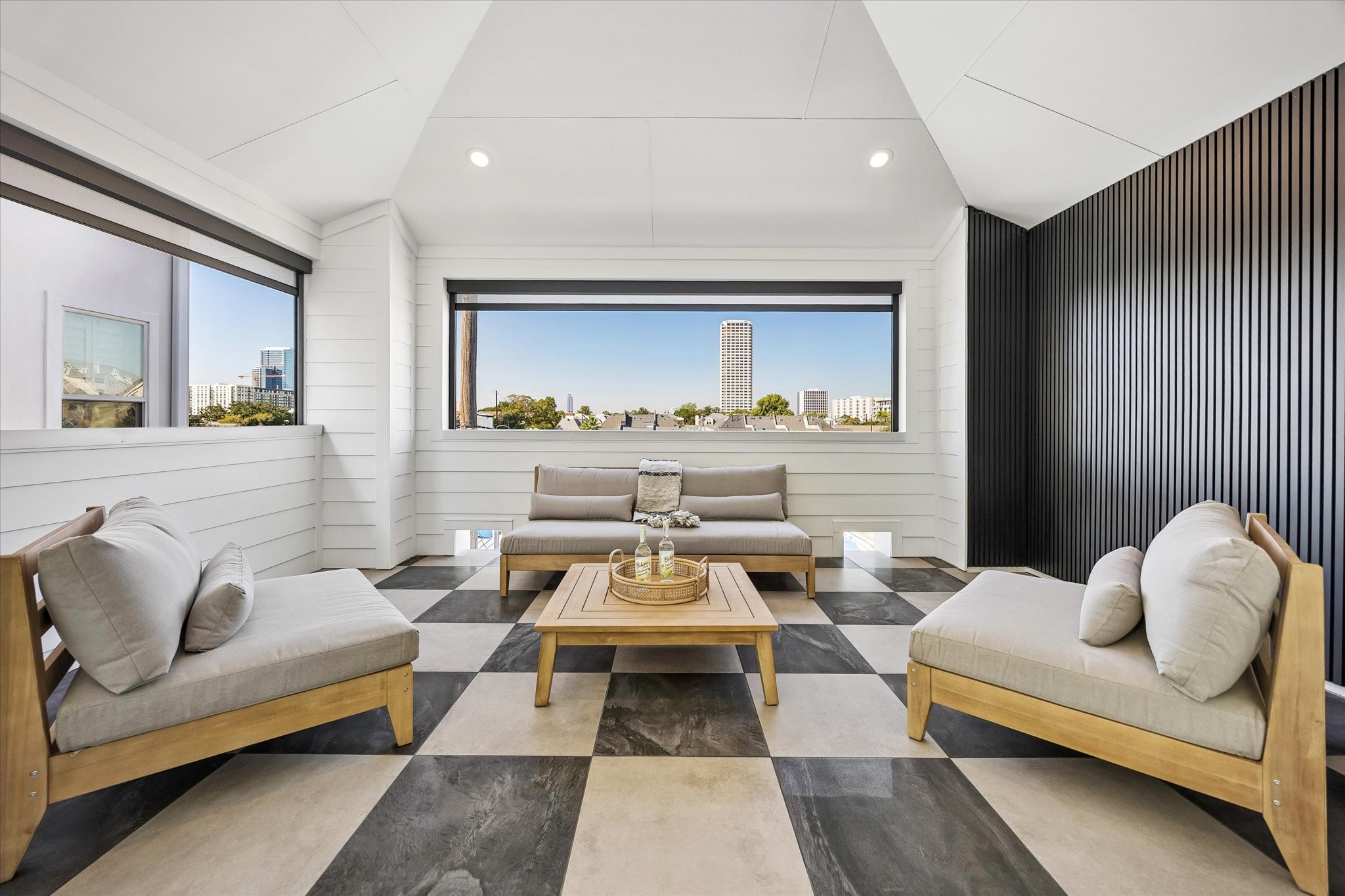 INCREDIBLE third-floor covered terrace offering fabulous outdoor living & entertaining! Soaring ceiling w/ modern ceiling fan, oversized checkered tile flooring, white horizontal siding & striking black vertical accent wall. Expansive openings offer elevated neighborhood & city views, creating the perfect setting for relaxing or hosting friends!