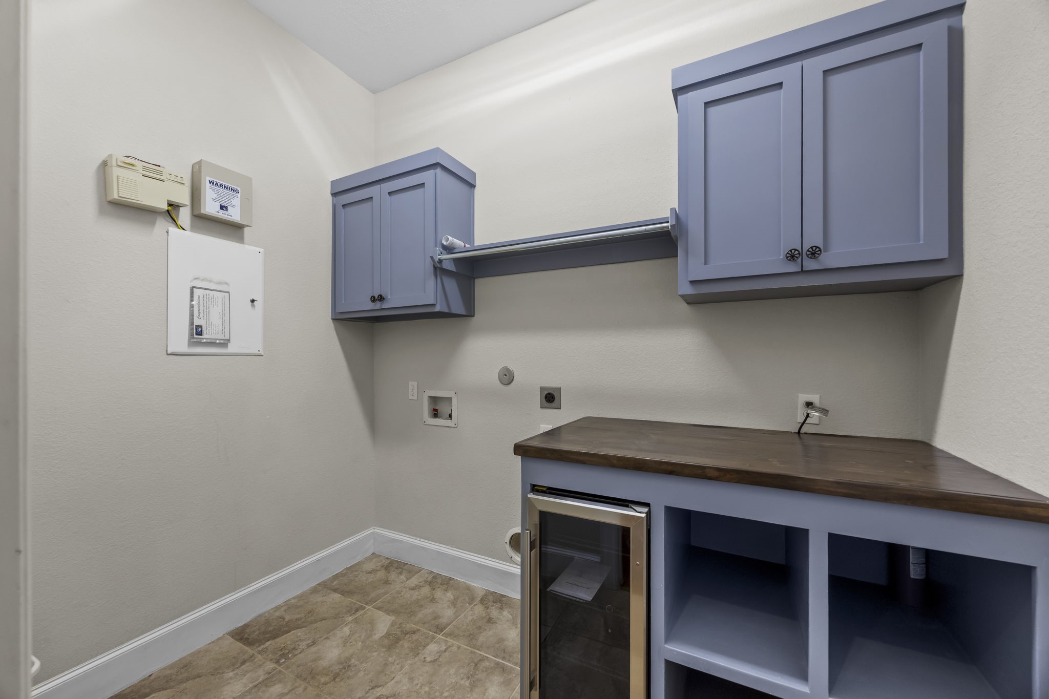 Functional utility room featuring custom cabinetry, a folding countertop, open storage cubbies, and a built-in beverage refrigerator. Washer and dryer connections and additional overhead storage make this a convenient space for everyday household needs.